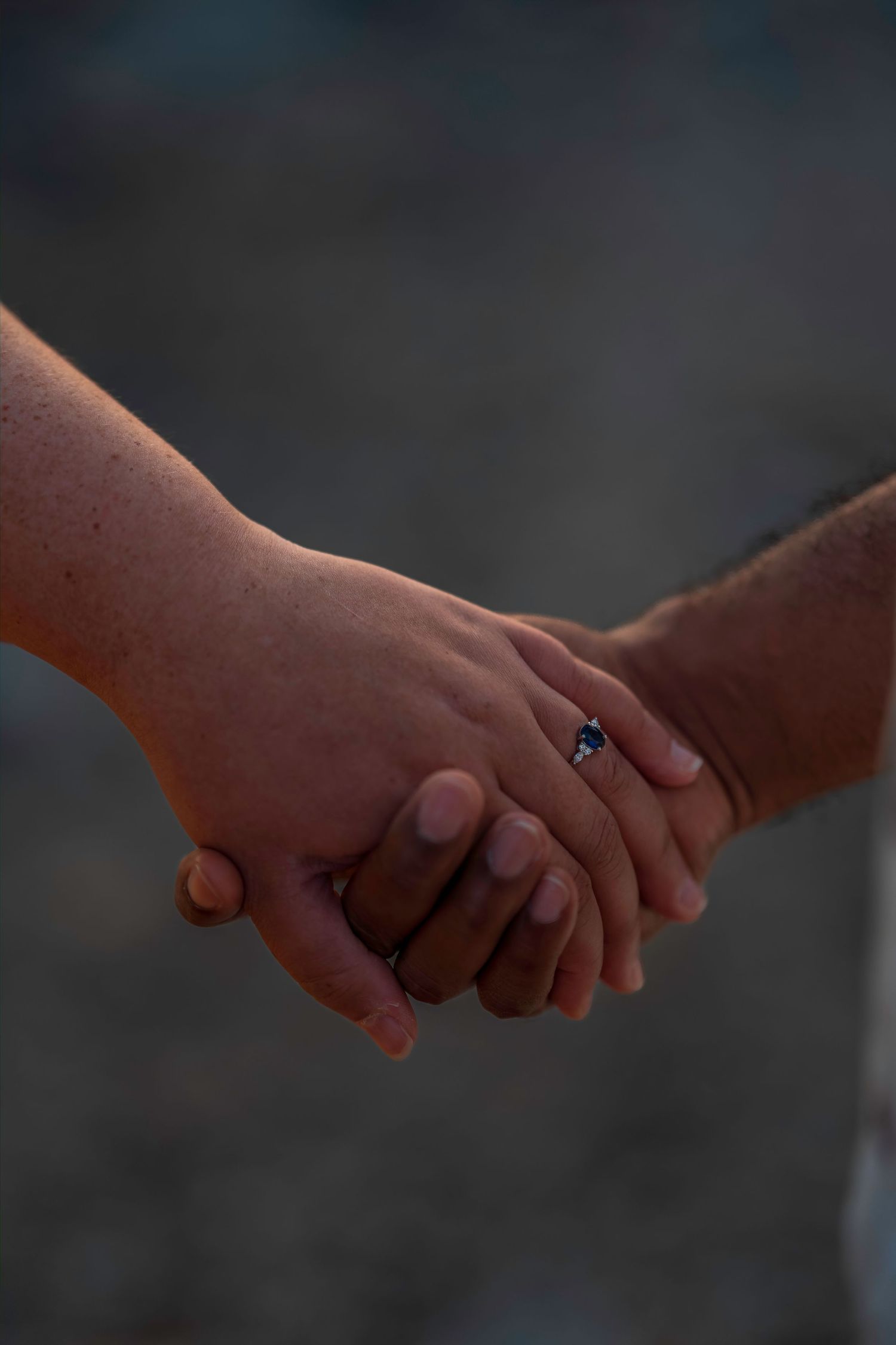Close-up of interracial couple holding hands with a blue sapphire engagement ring visible on finger.