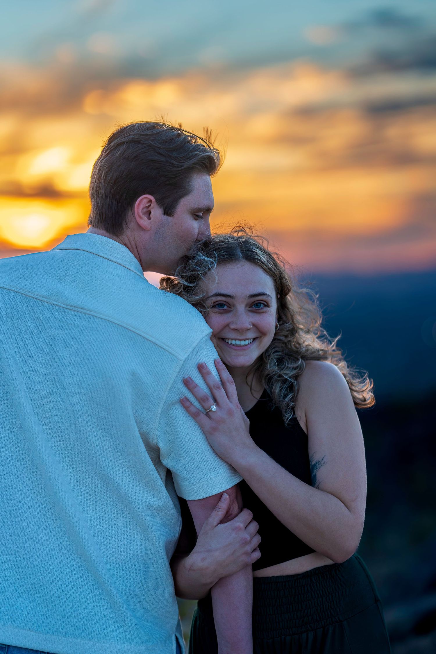 Happy woman showing engagement ring while embraced by partner at sunset.