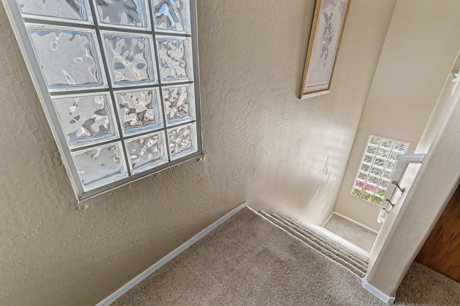 Carpeted staircase landing with glass block window allowing natural light in a neutral-toned home interior.
