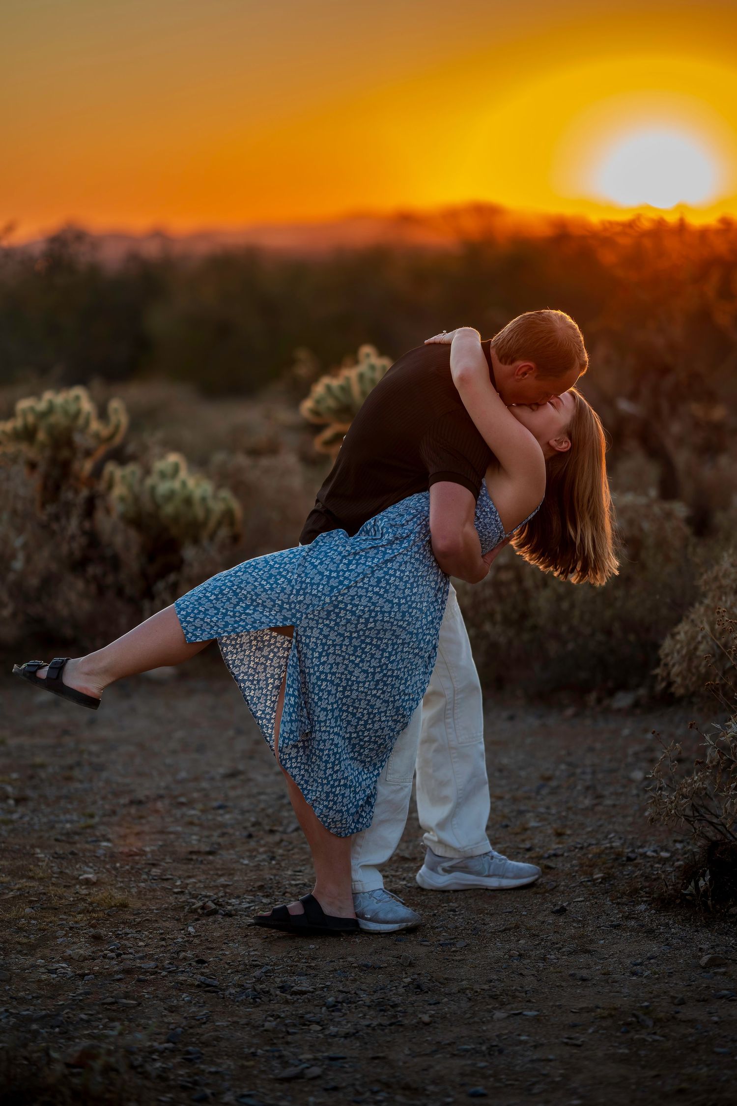 Couple sharing a romantic dip kiss at golden sunset in desert landscape with cacti.