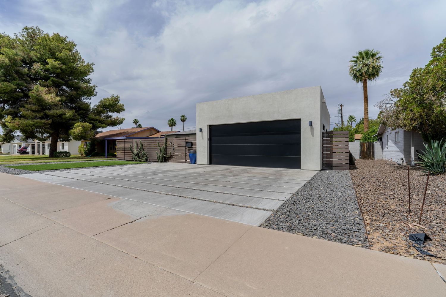 Modern home exterior with double garage, concrete driveway, desert landscaping, and stucco facade under cloudy skies.