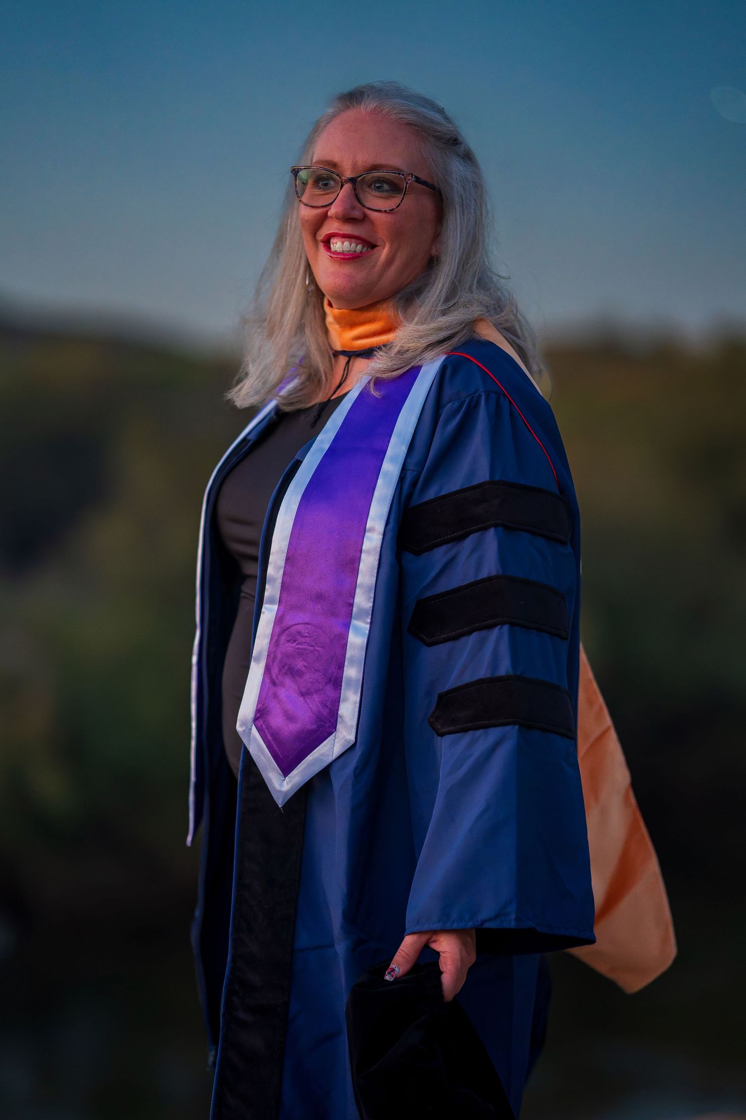 Graduate in ceremonial academic dress poses during golden hour photo shoot.