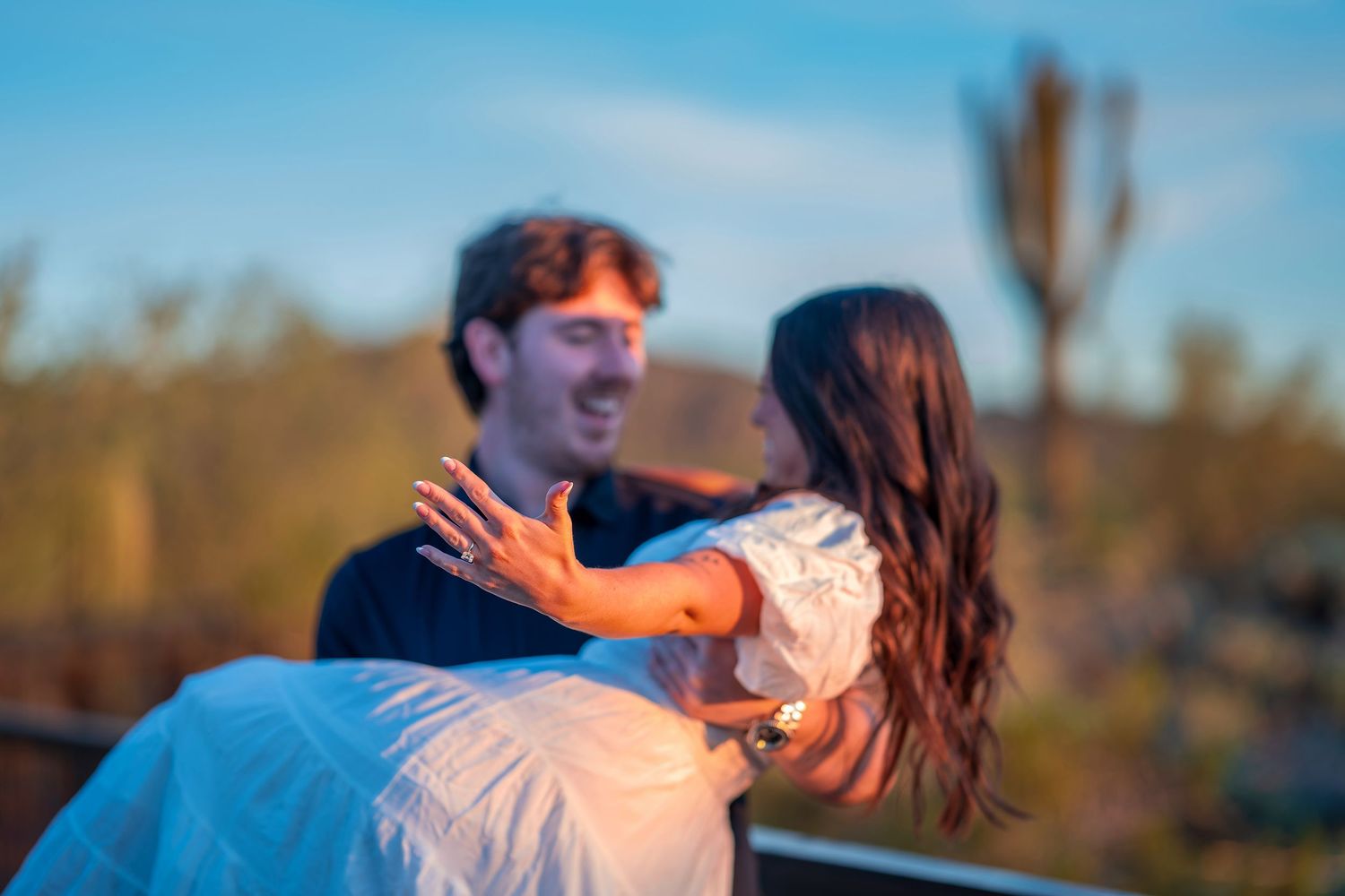 Candid moment of a couple laughing together during golden hour with desert landscape behind them.