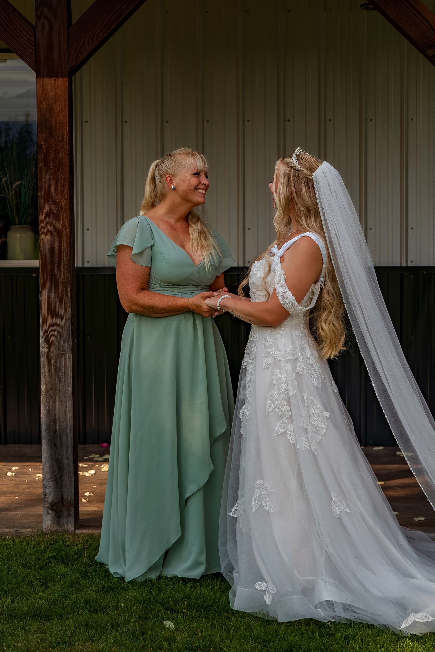 Two women share an emotional embrace during a wedding, with one in a sage green dress and one in a white gown.