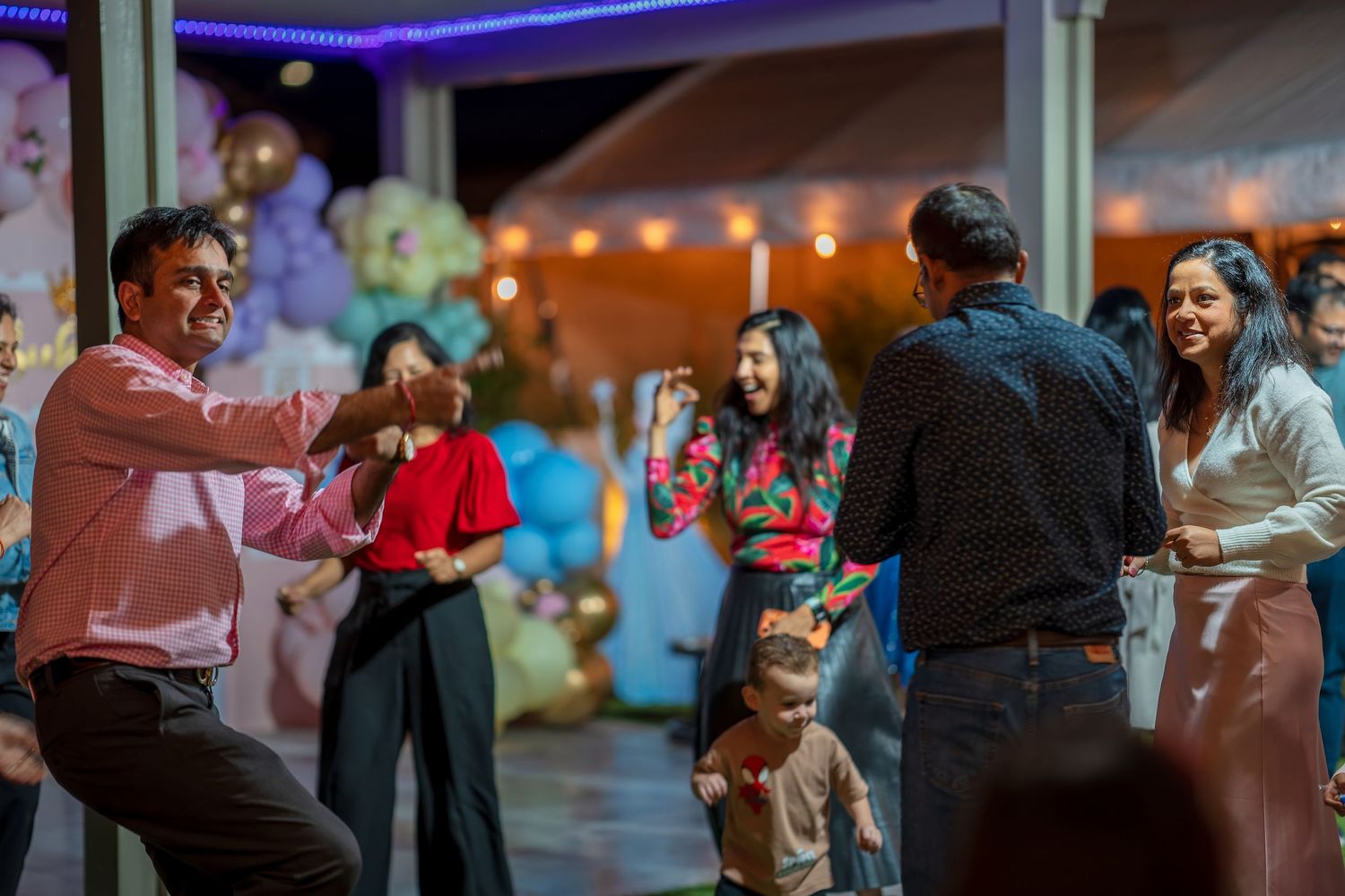 Partygoers dancing under purple lighting at an outdoor evening celebration.