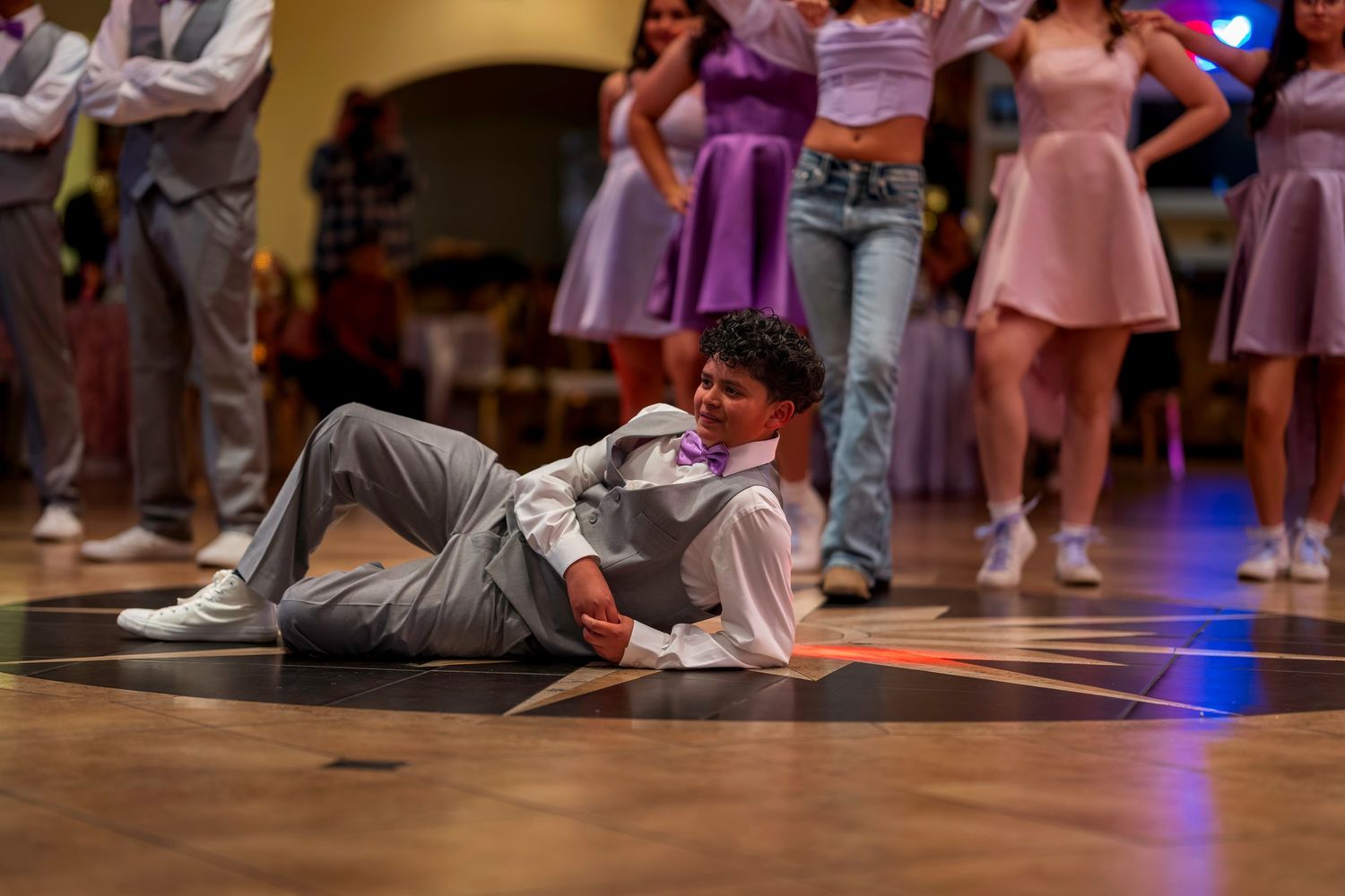 Young man in gray suit performing dance floor moves at a formal prom or quinceañera celebration.
