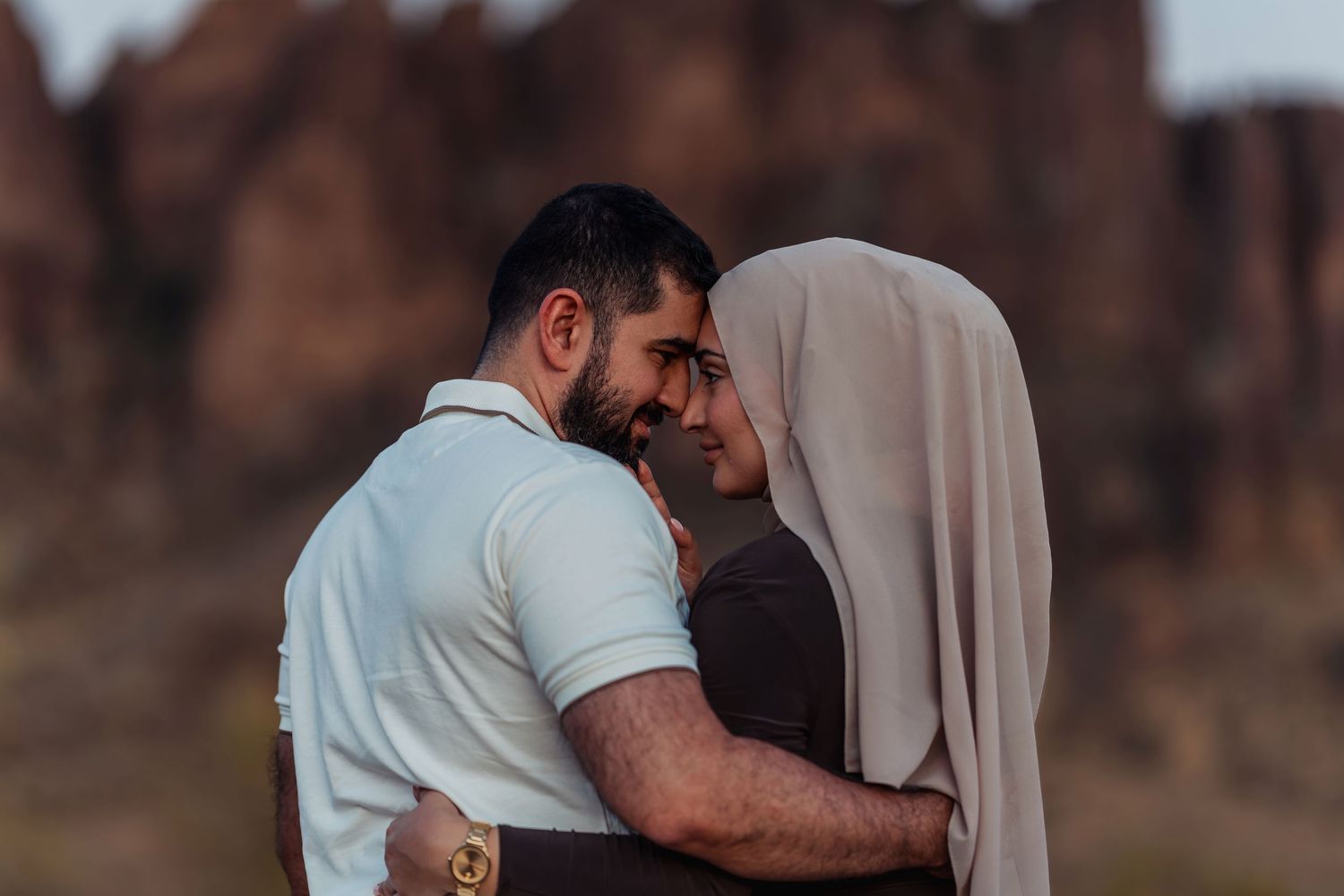 A couple sharing an intimate moment, the woman wearing a hijab, with rocky formations in the background.