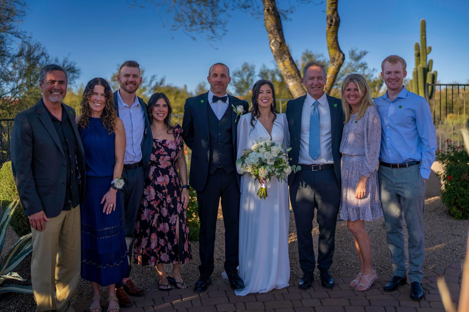 Wedding couple in formal attire poses with eight family members outdoors in desert landscape.