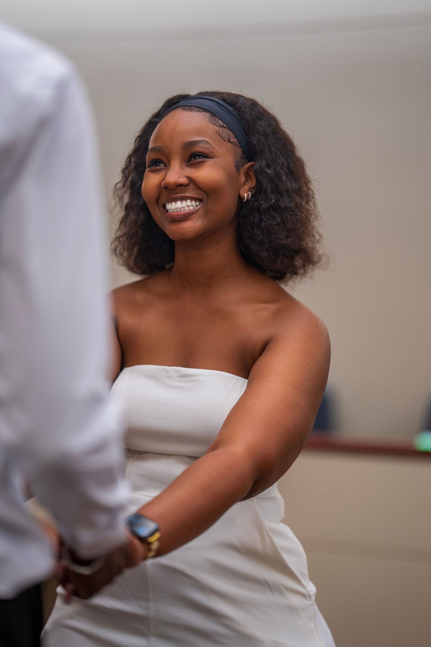 A radiant bride in a strapless white dress smiles while holding hands with her groom.