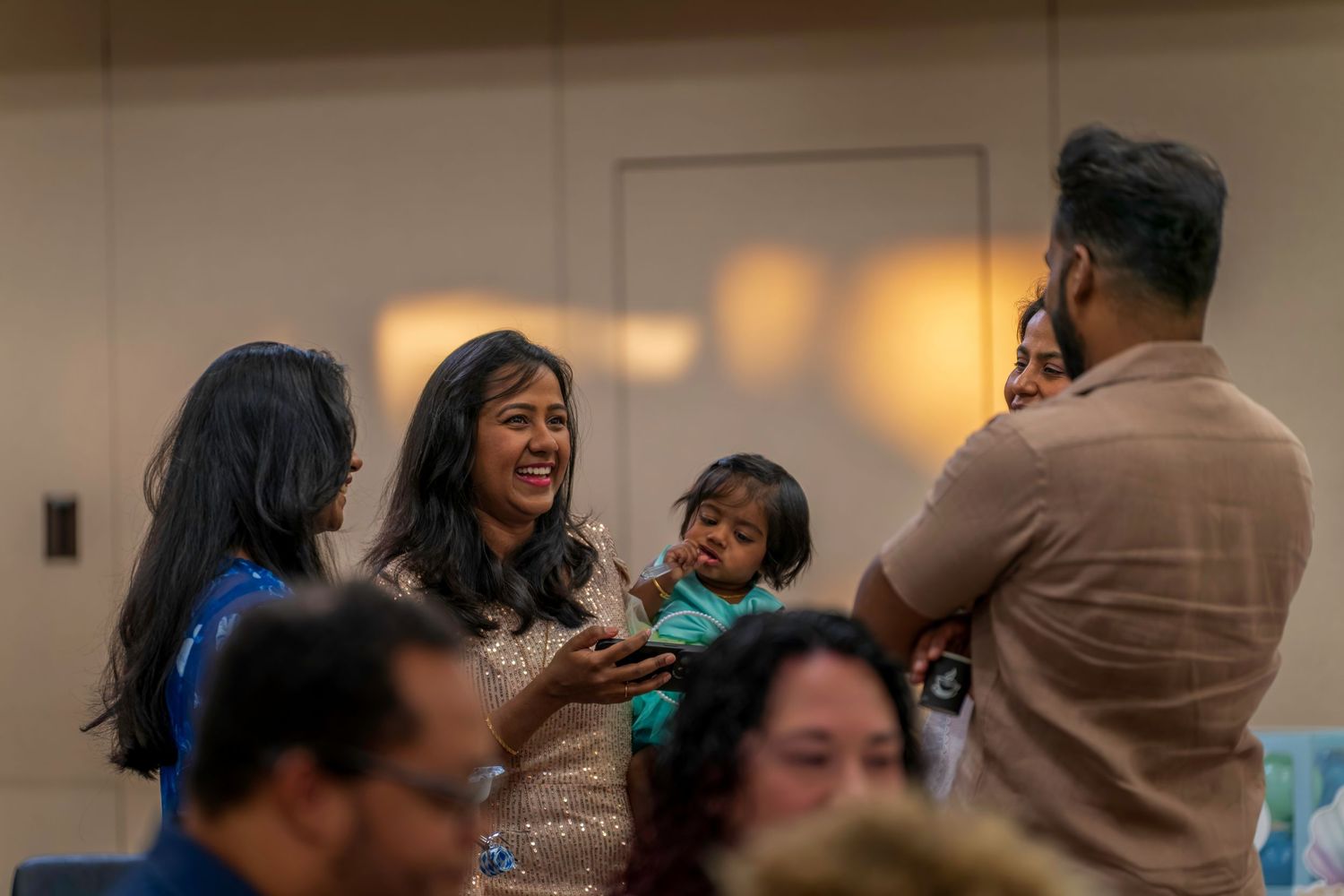 Family smiling and holding a baby at a first birthday celebration party indoors.