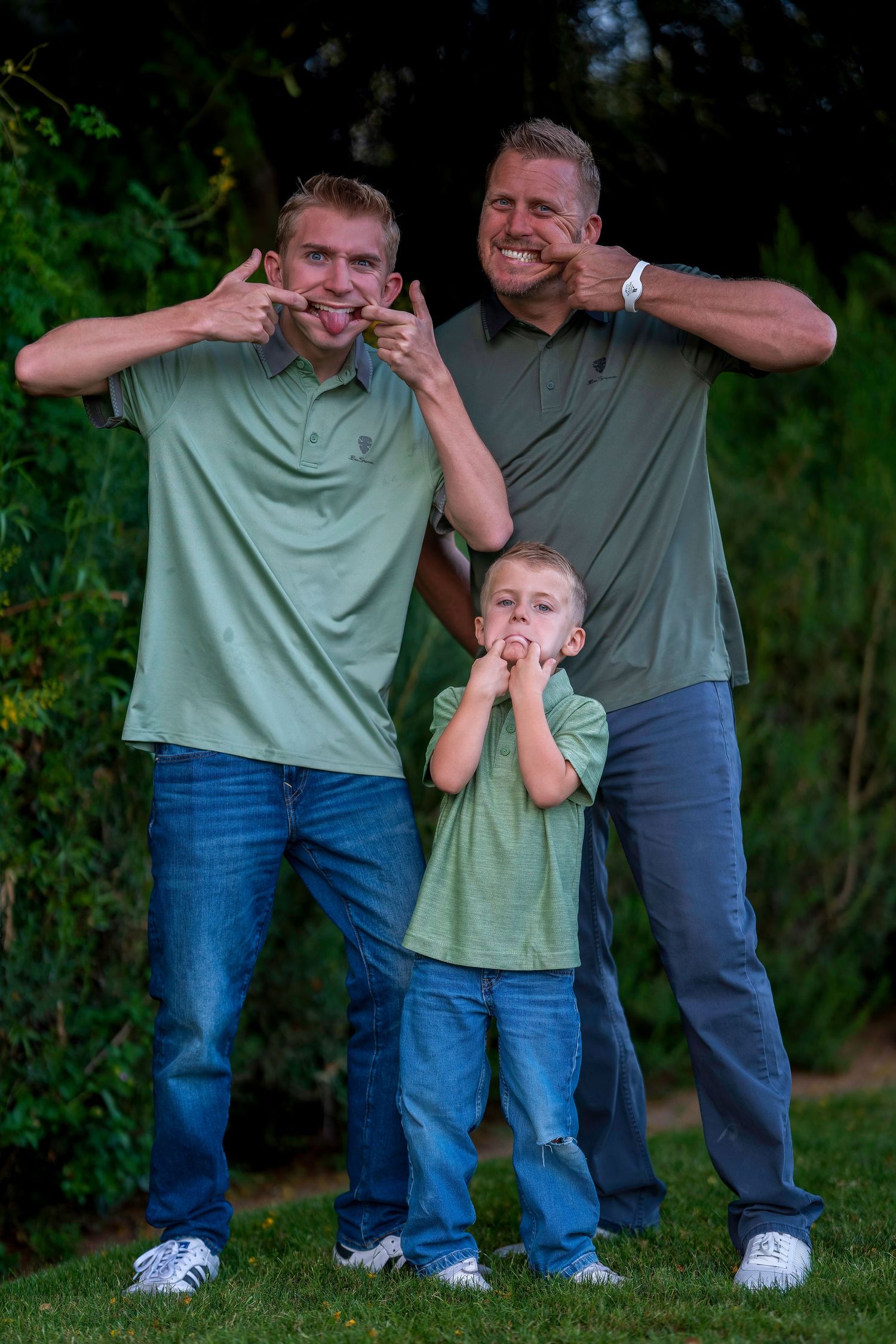 Three males in matching green shirts make funny faces outdoors.