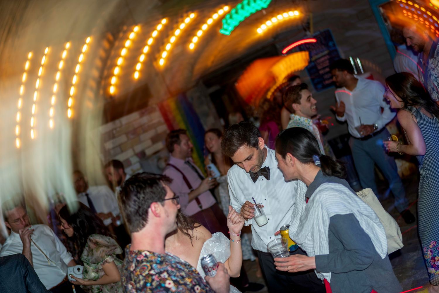 Lively indoor party scene with guests socializing under warm string lights in a vibrant venue.