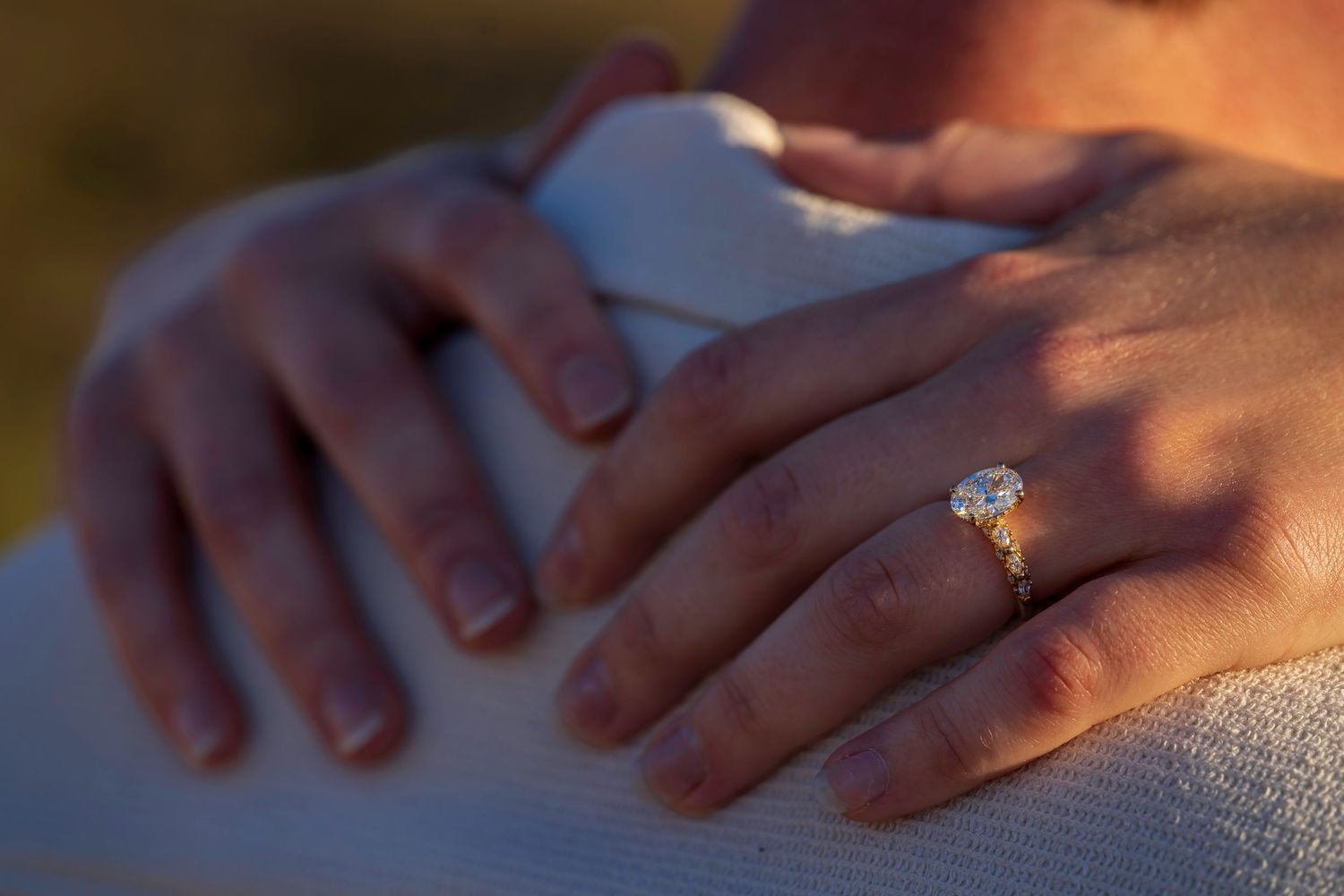 Close-up of a diamond engagement ring on a woman's hand in golden light.