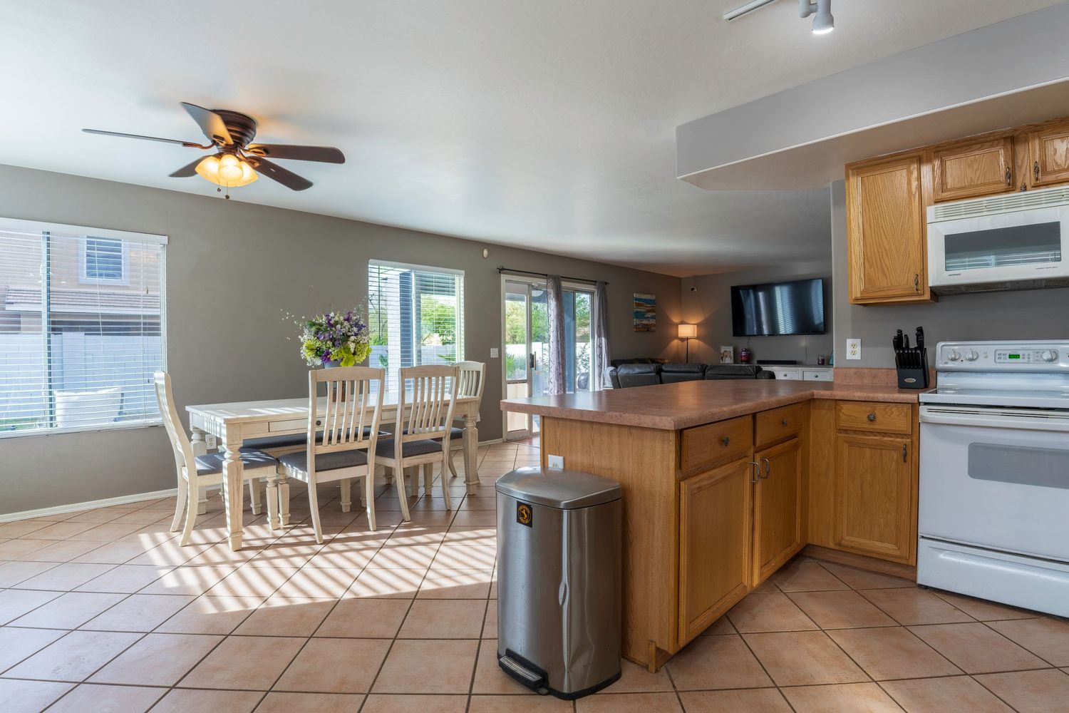 Open kitchen and dining area with oak cabinets, white appliances, tile floors, and sliding glass patio doors.