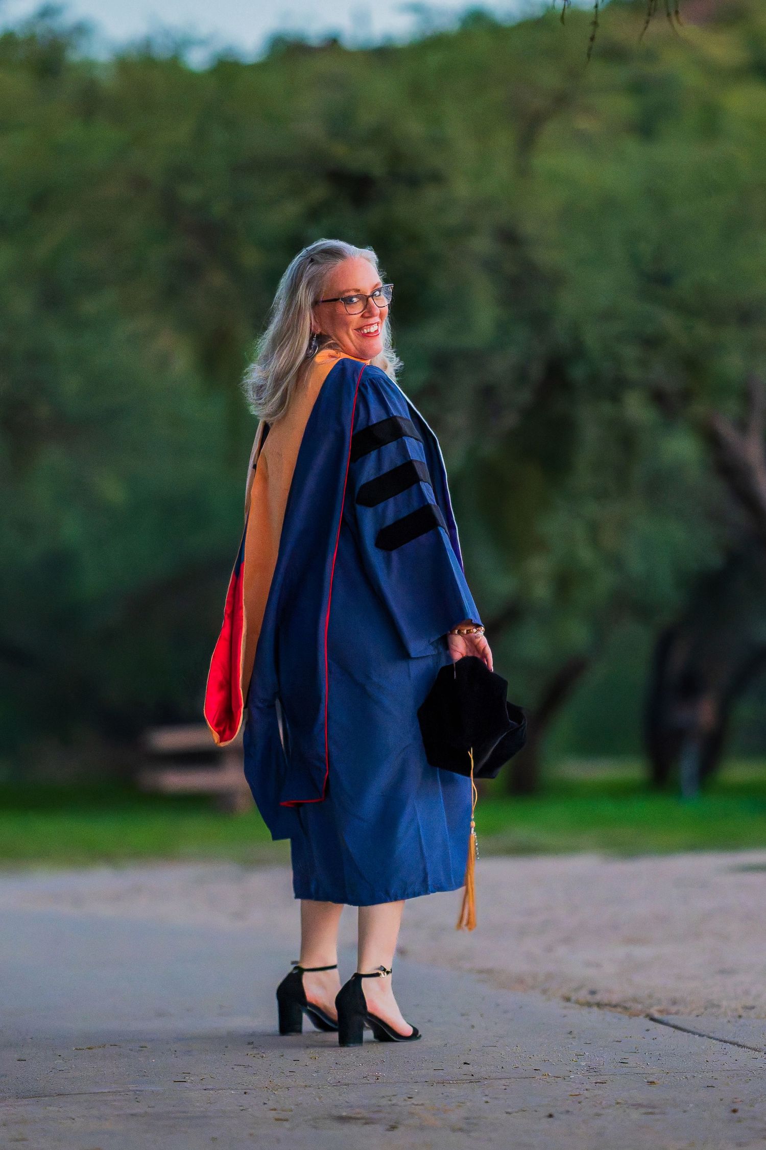 Graduate walking outdoors wearing traditional academic regalia with colorful stole.