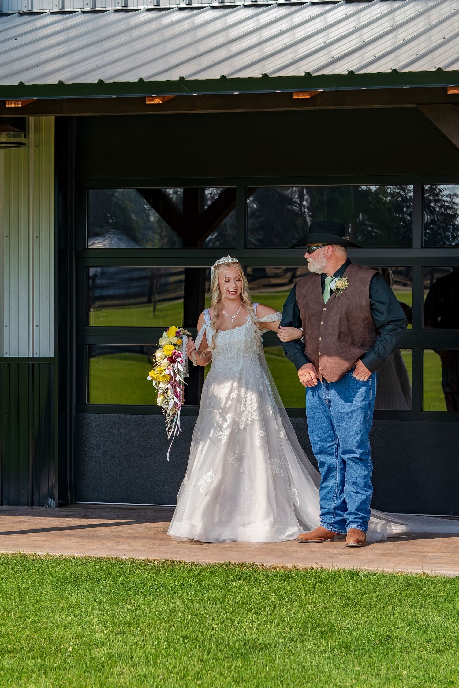 Wedding party gathered under covered pavilion with green lawn in foreground.