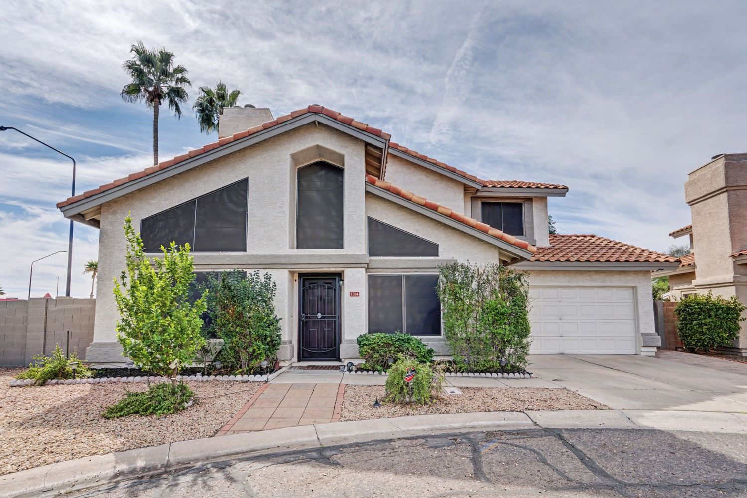 Two-story stucco home with tile roof, desert landscaping, attached garage, and palm tree in Arizona suburb.