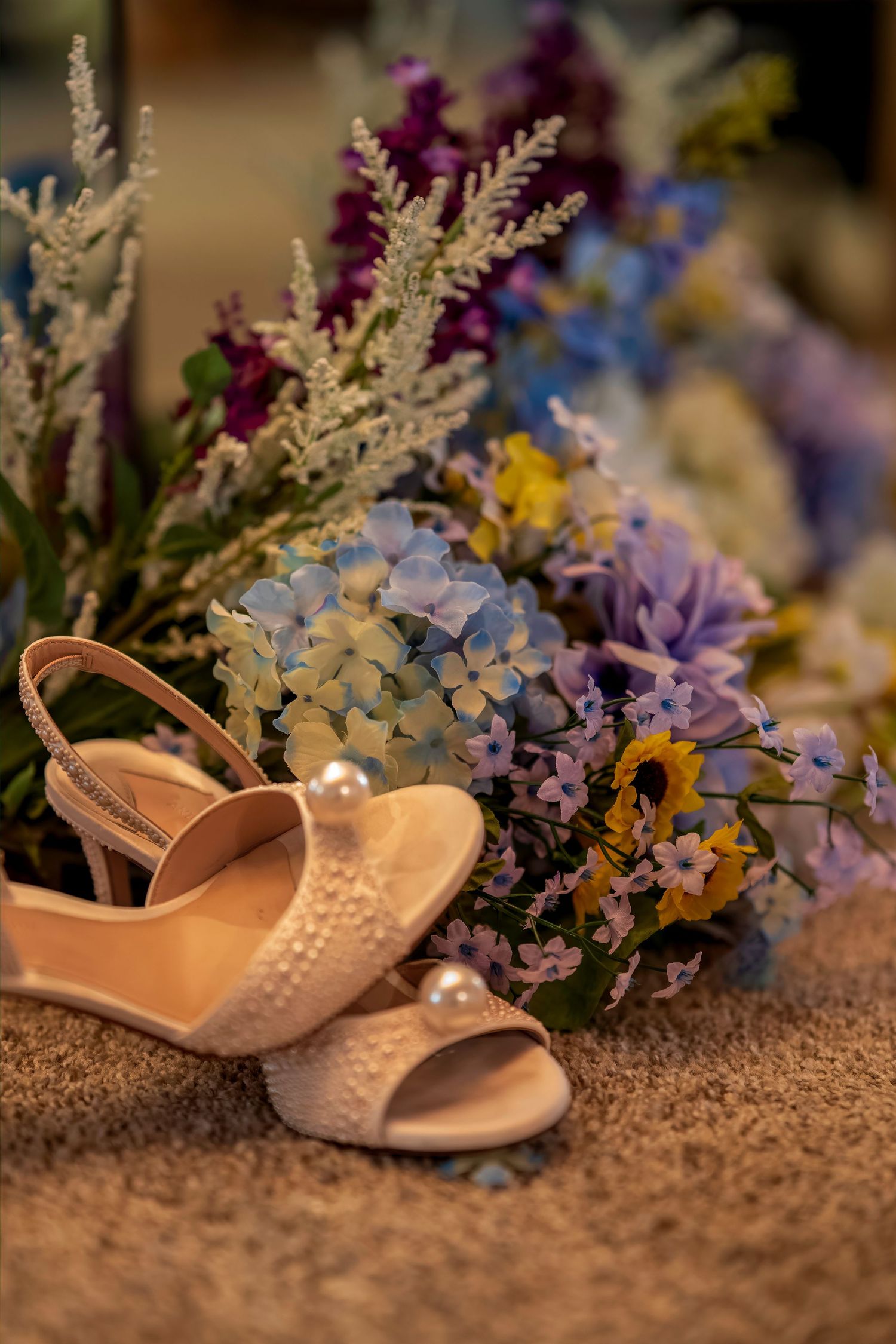 Elegant pearl-adorned bridal heels resting beside a colorful wedding bouquet of purple, blue, and yellow flowers.