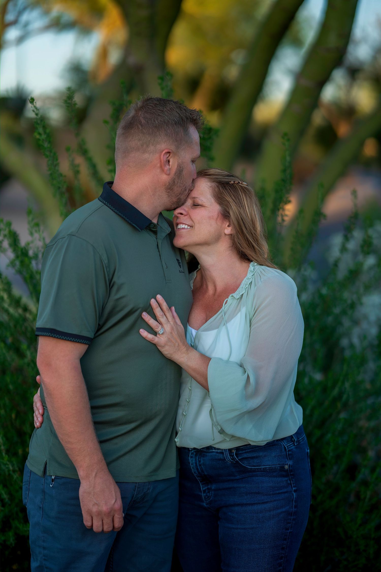 Couple sharing a tender kiss outdoors surrounded by green desert plants in golden hour light.