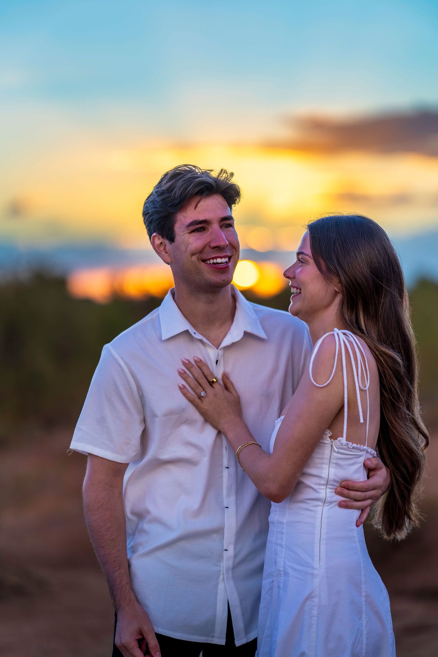 A couple shares joyful laughter during their desert engagement session at golden hour.