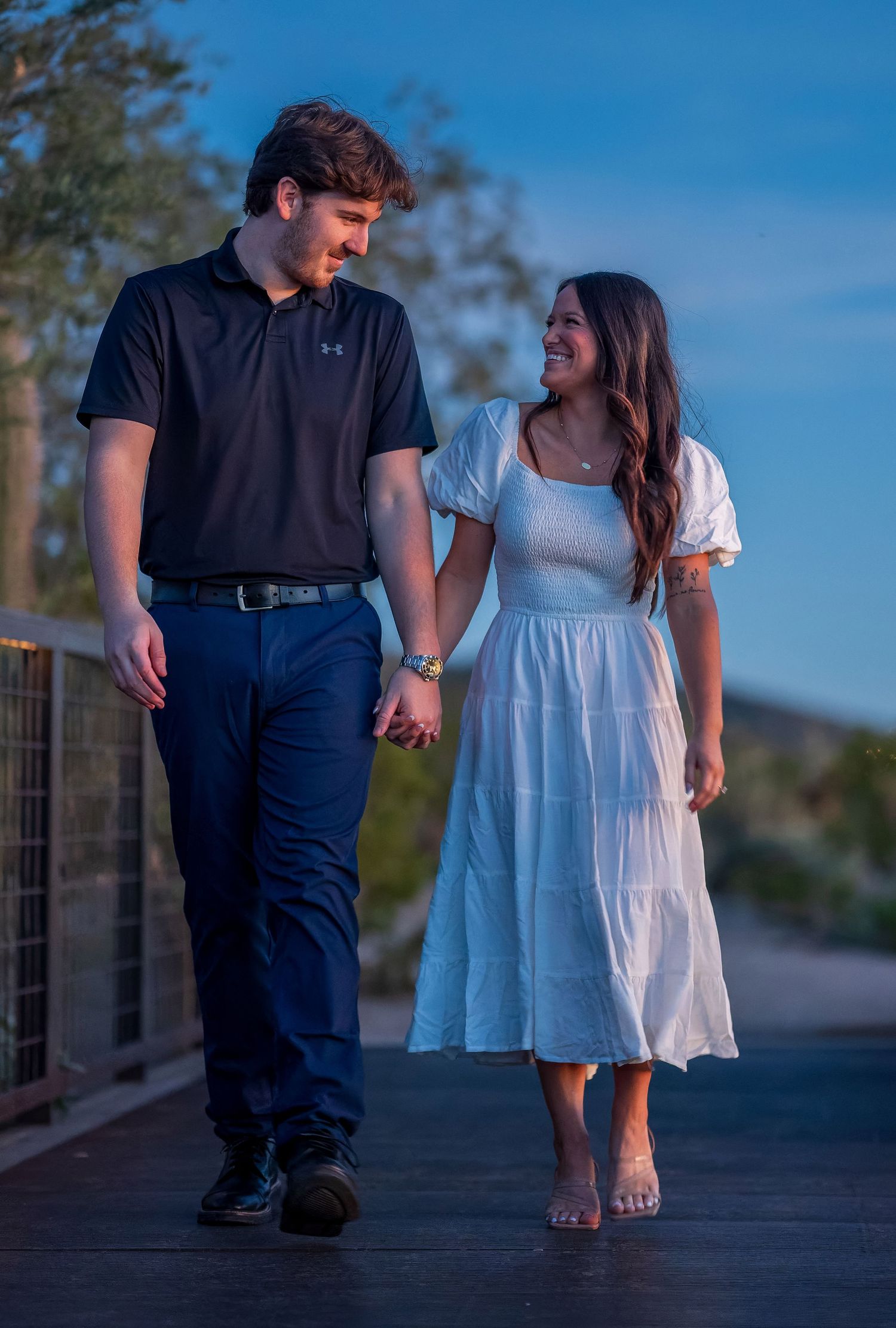 Couple walks together on wooden boardwalk during blue hour photography session.