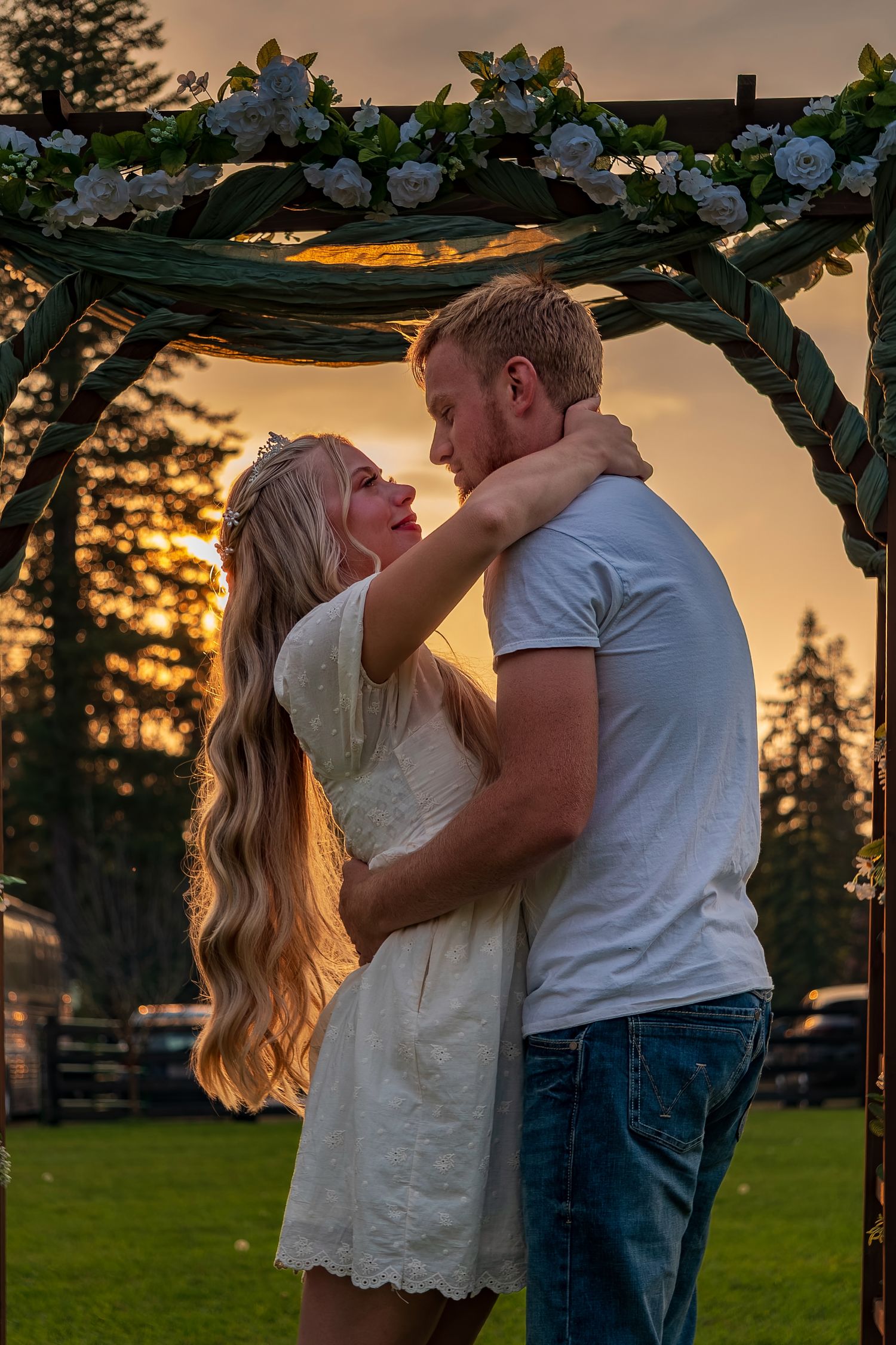 Romantic couple sharing an intimate moment under a floral arch during golden hour sunset.