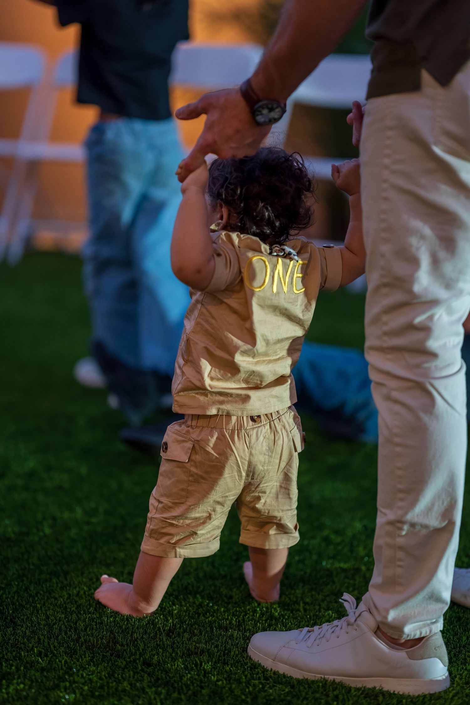 Small feet in white shoes standing on grass during an outdoor celebration.
