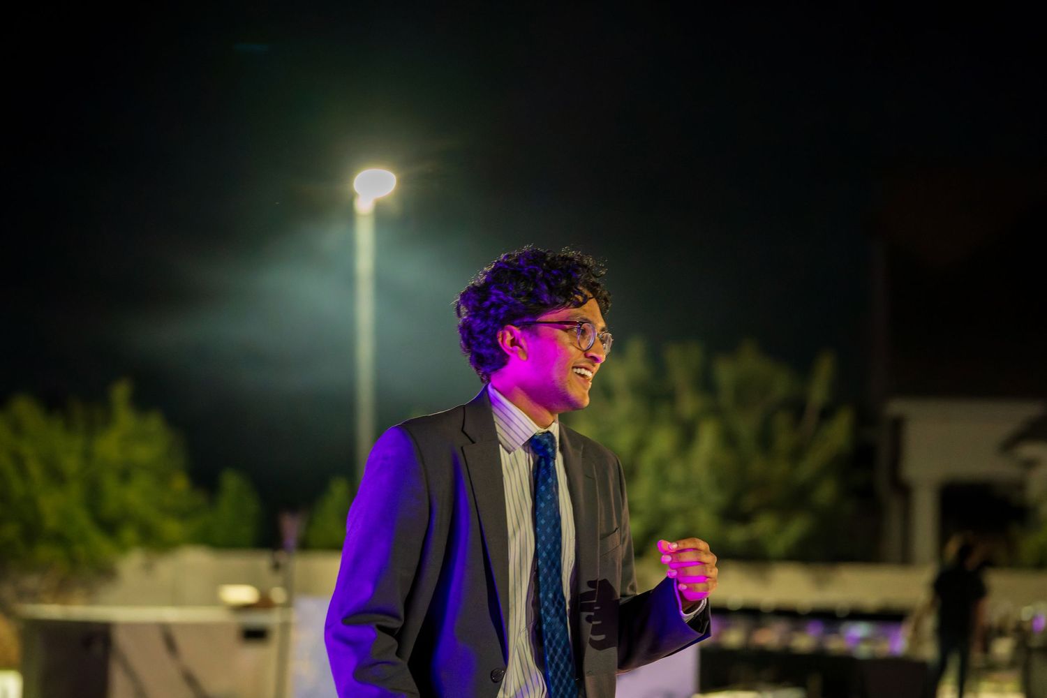 Person in formal attire illuminated by colorful lighting at outdoor nighttime event.