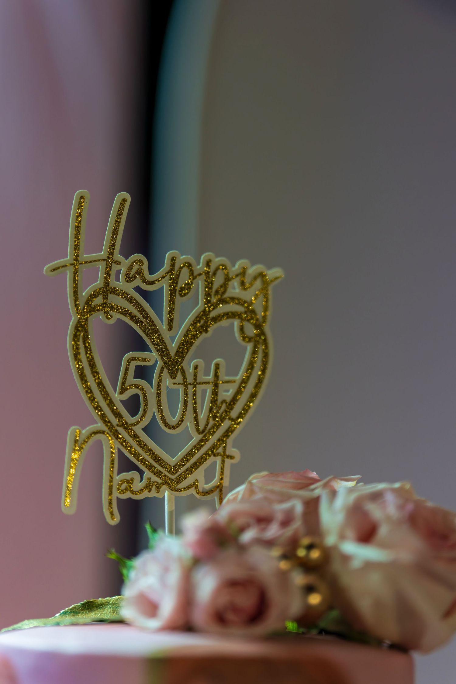 Gold glitter cake topper reading 'Happy' adorns a pink frosted cake.