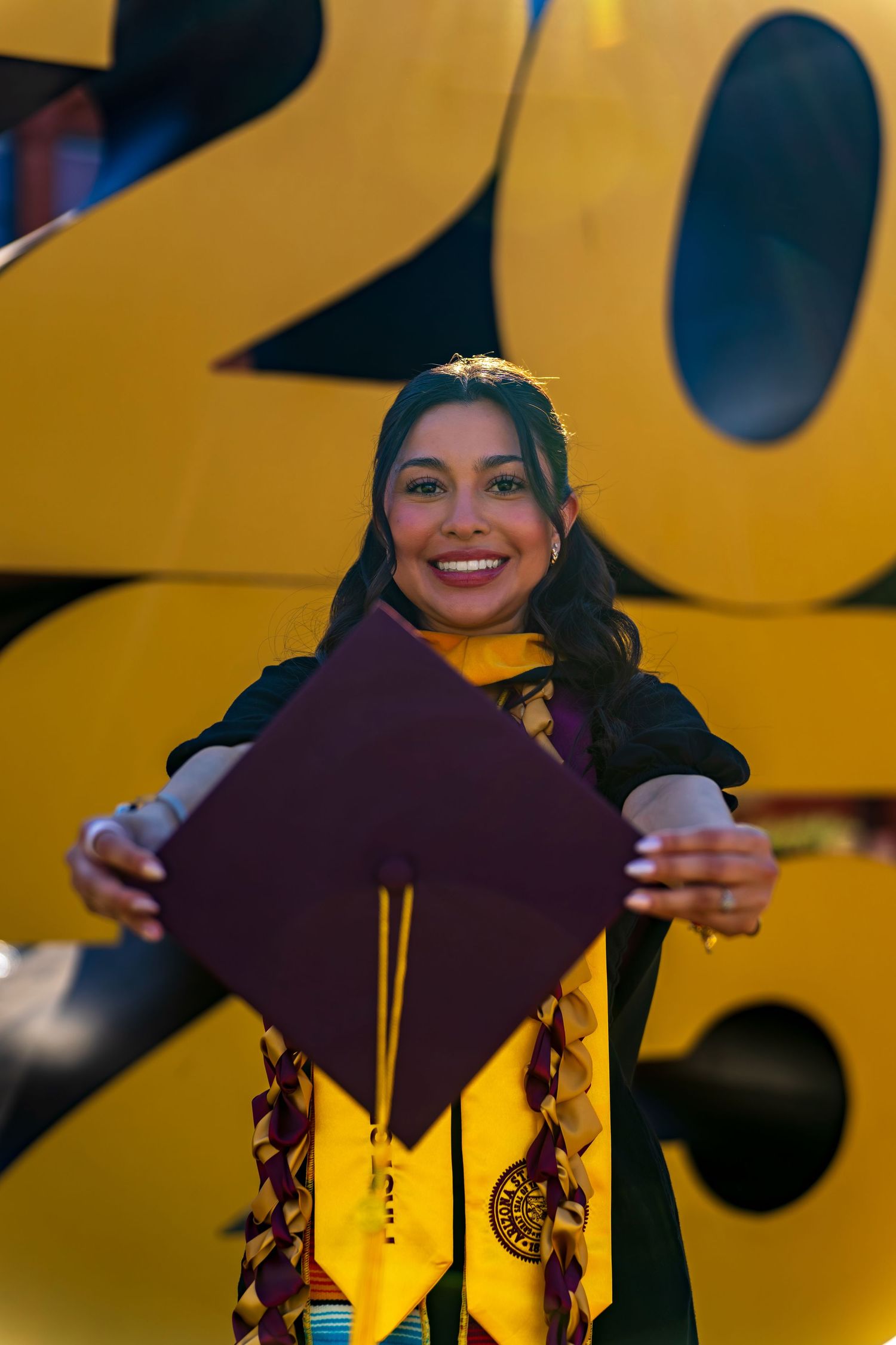 Graduate holds up diploma cover against large gold 2023 numbers in background.
