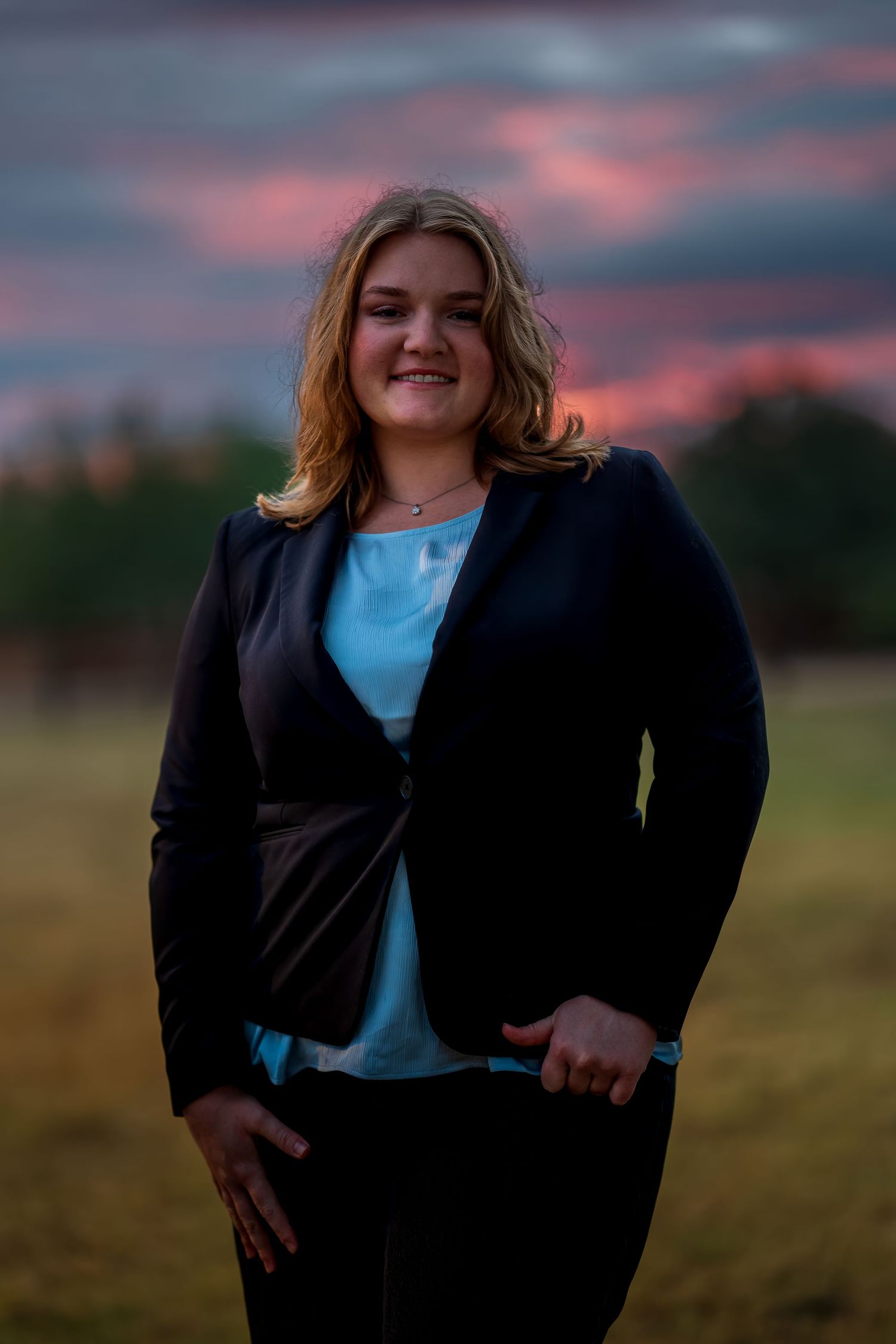 Casual outdoor portrait session with dramatic cloudy sunset backdrop.