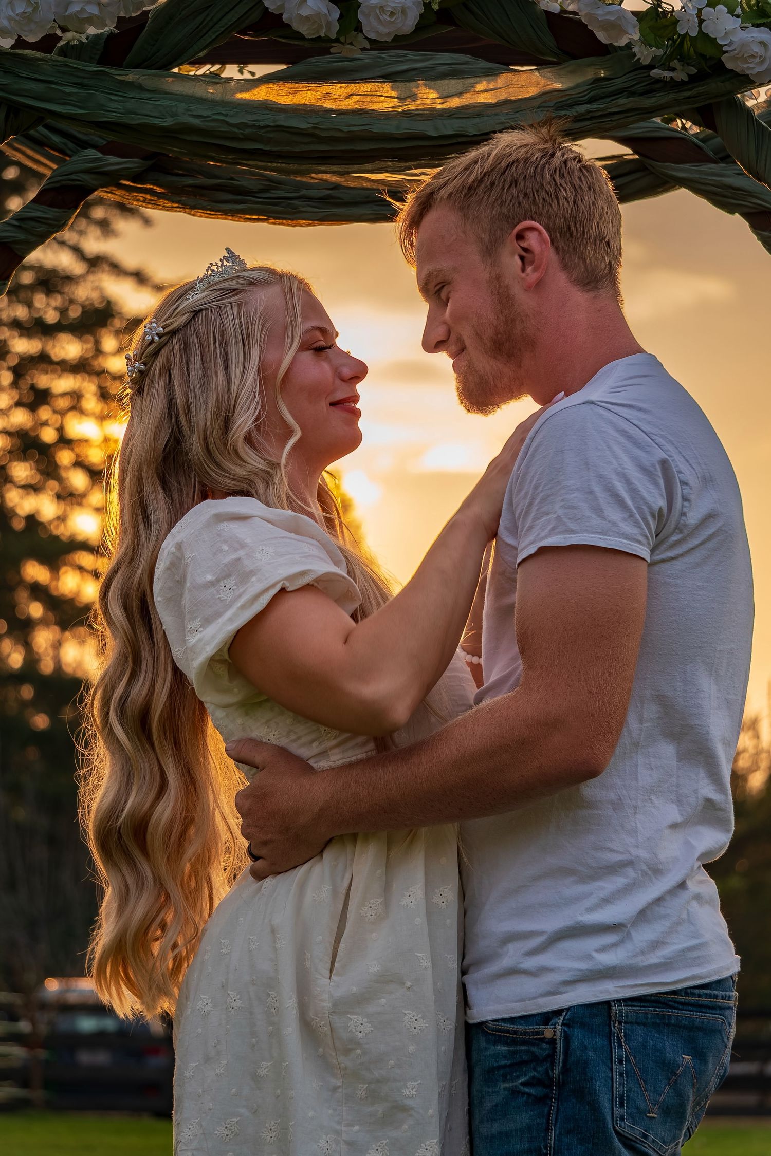 Tender moment between couple against warm sunset backdrop under garden trellis.