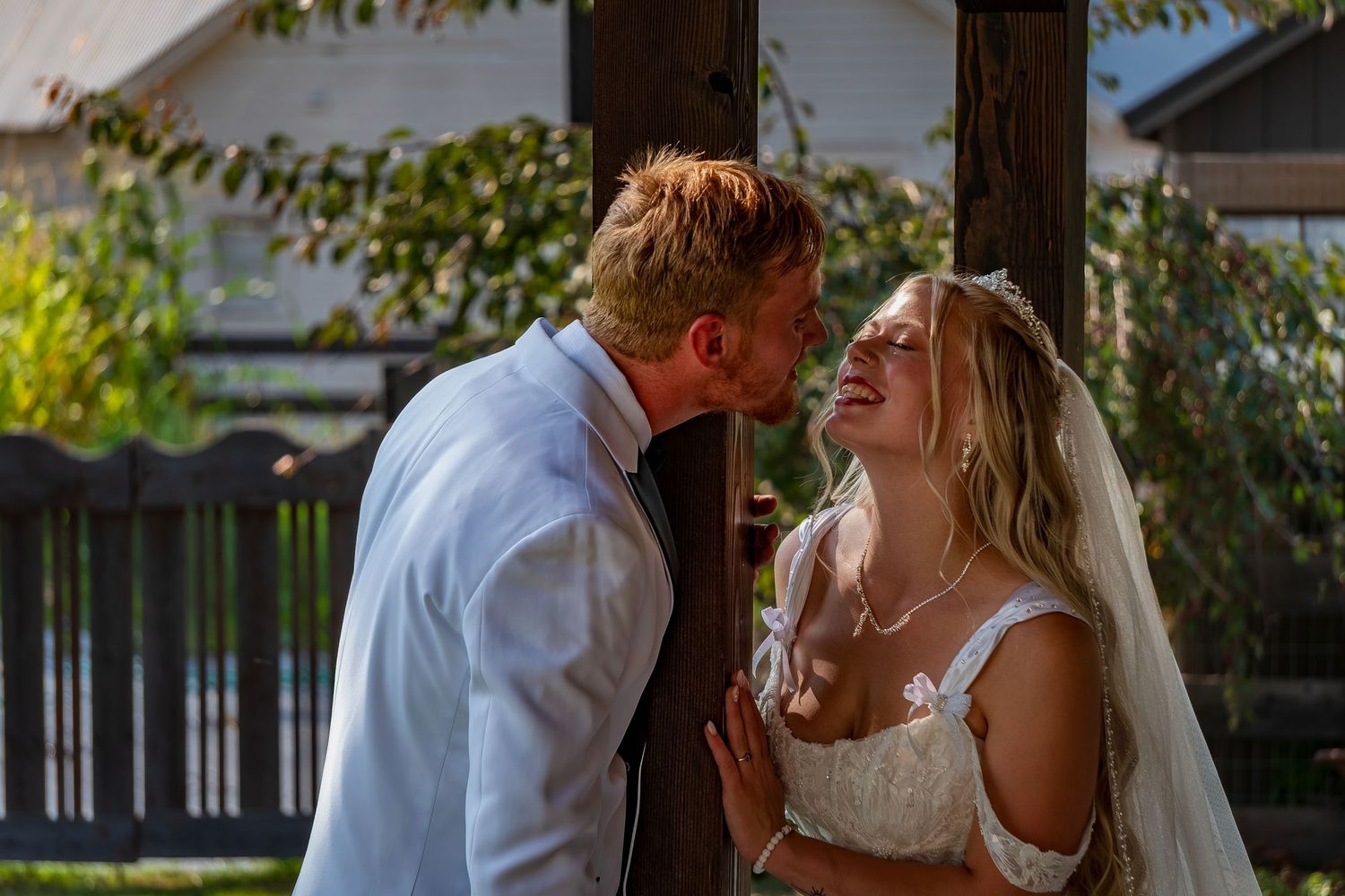 Romantic moment between newlyweds under wooden pergola during golden hour.