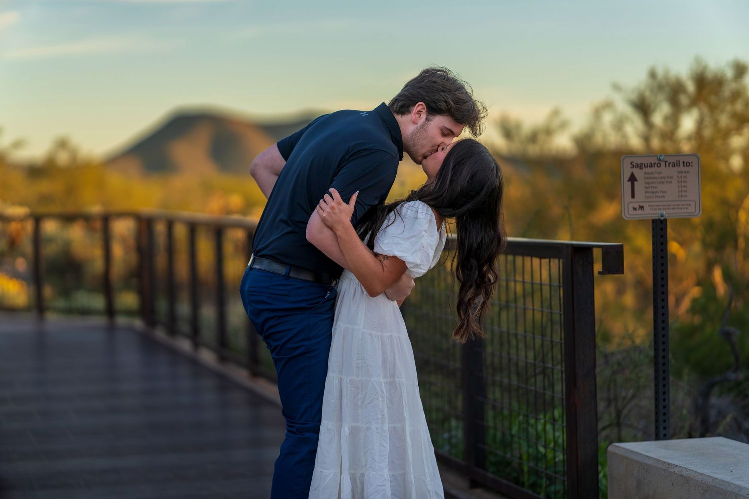 A romantic embrace between a newly engaged couple on a desert overlook during golden hour.