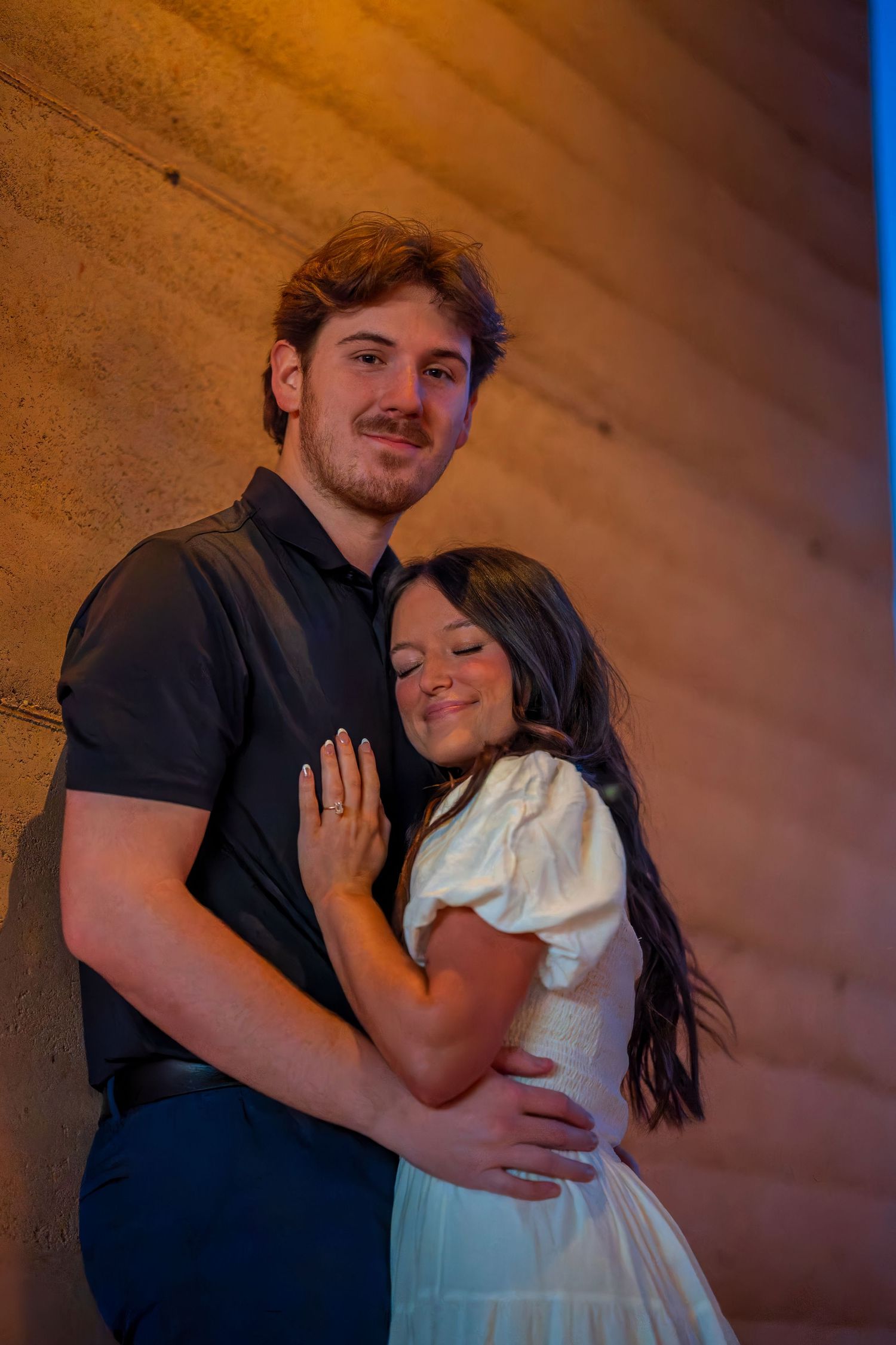 Sweet couple poses against textured wall during golden hour photography session.