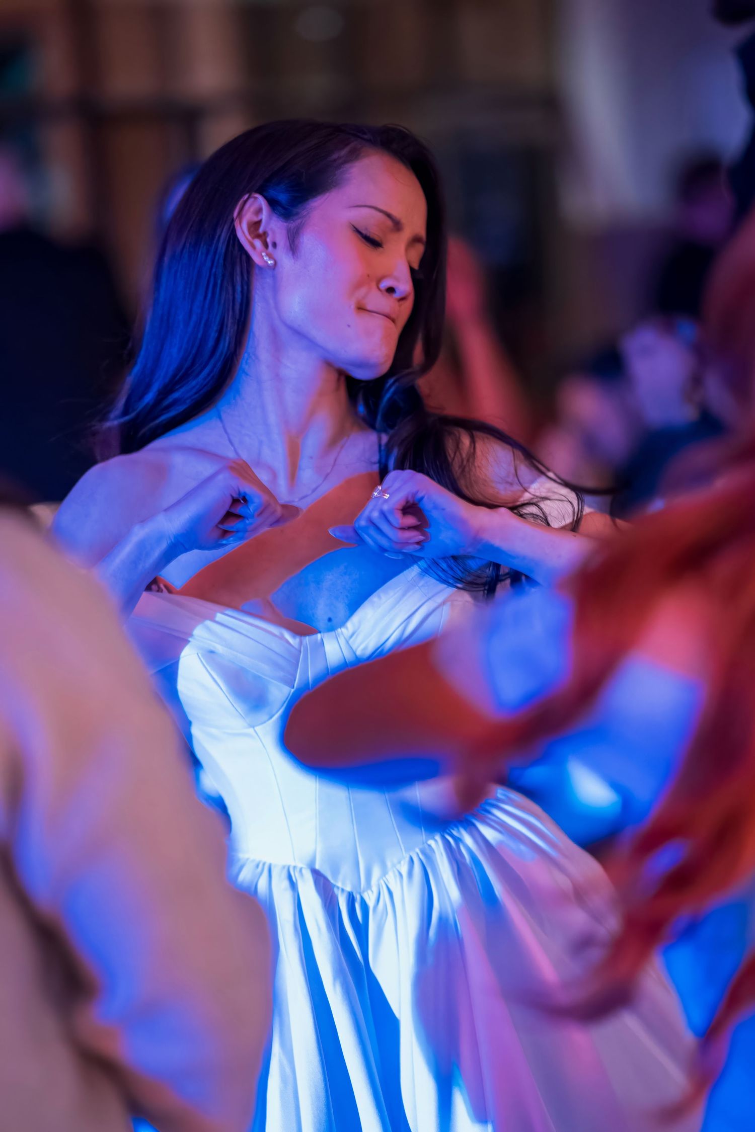 Woman in white dress dances joyfully under blue lighting at indoor celebration.