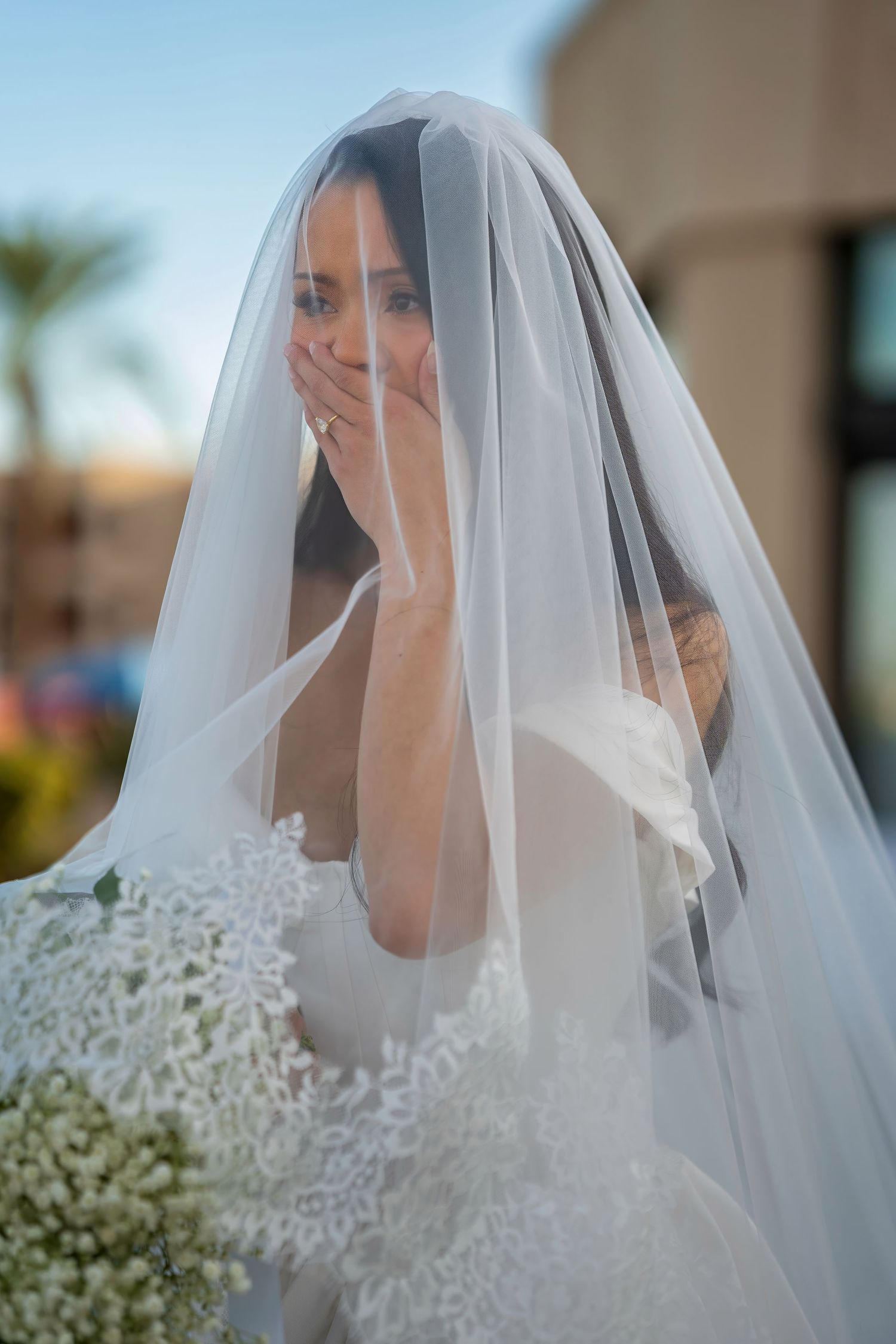 A joyful bridal portrait showing an emotional moment through a delicate veil.