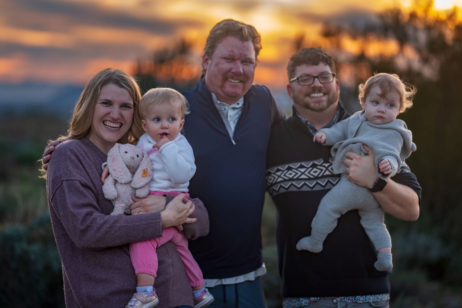 Family portrait session featuring warm embraces against dramatic sunset sky.
