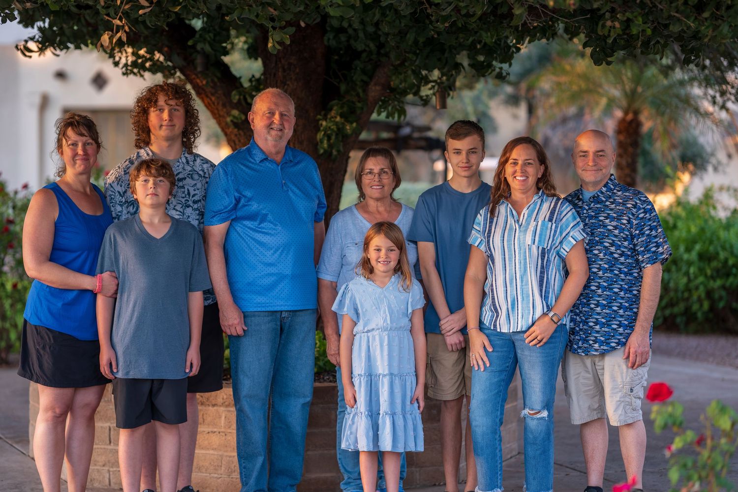Extended family wearing coordinated blue outfits poses together outdoors during golden hour.