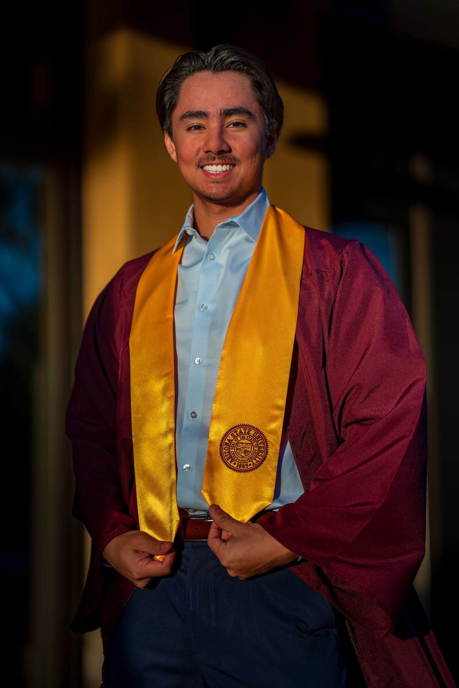 Graduate wearing maroon cap and gown with gold honors stole during graduation ceremony.