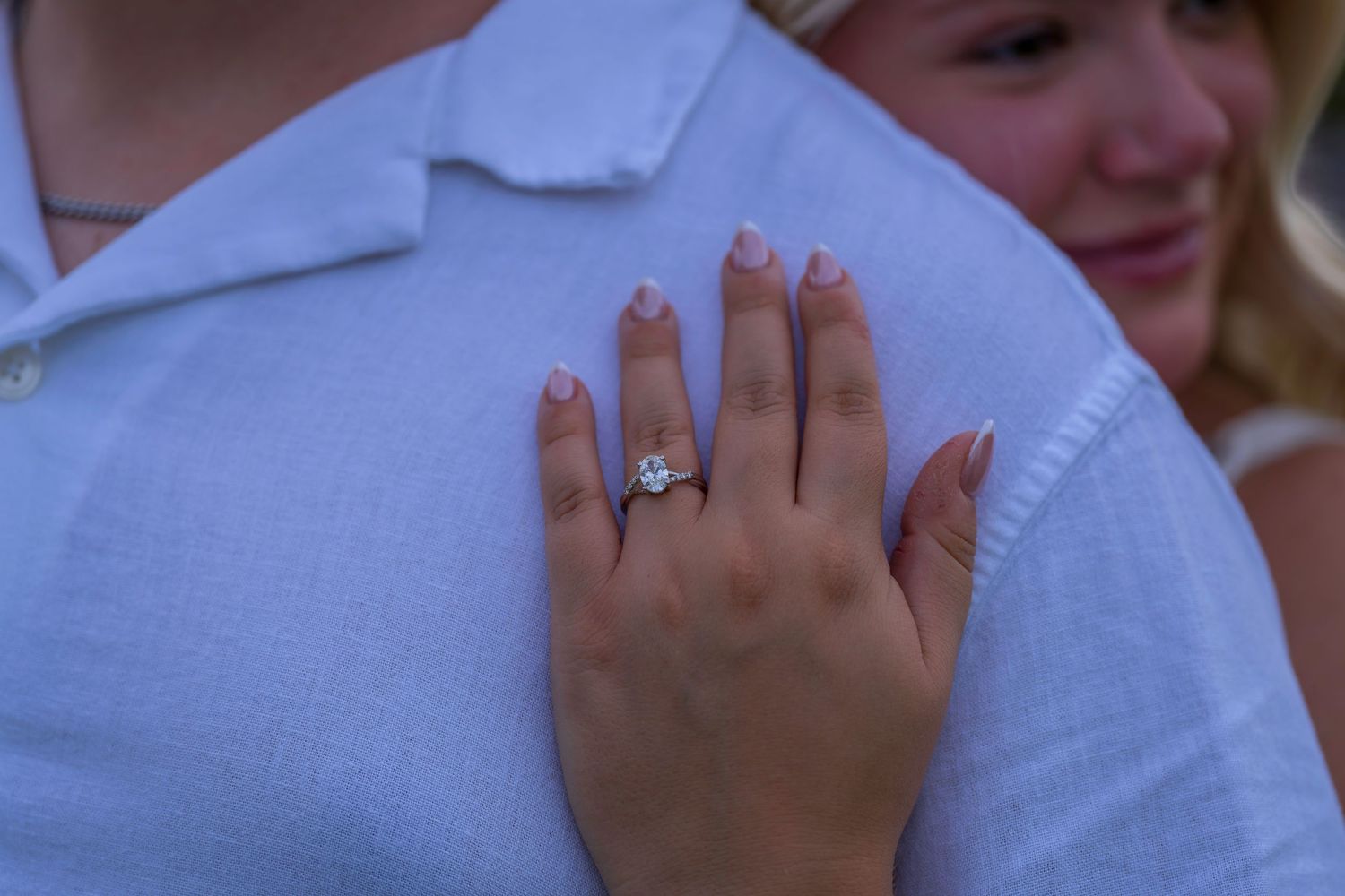 Close-up of a sparkling diamond engagement ring on a woman's hand resting on a man's blue shirt.