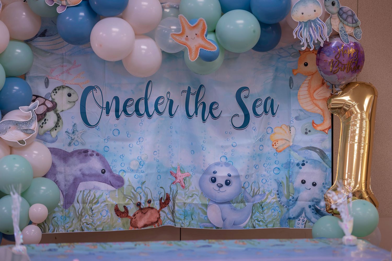 Under the Sea first birthday party backdrop with balloons, sea creatures, and a gold number 1 balloon centerpiece.