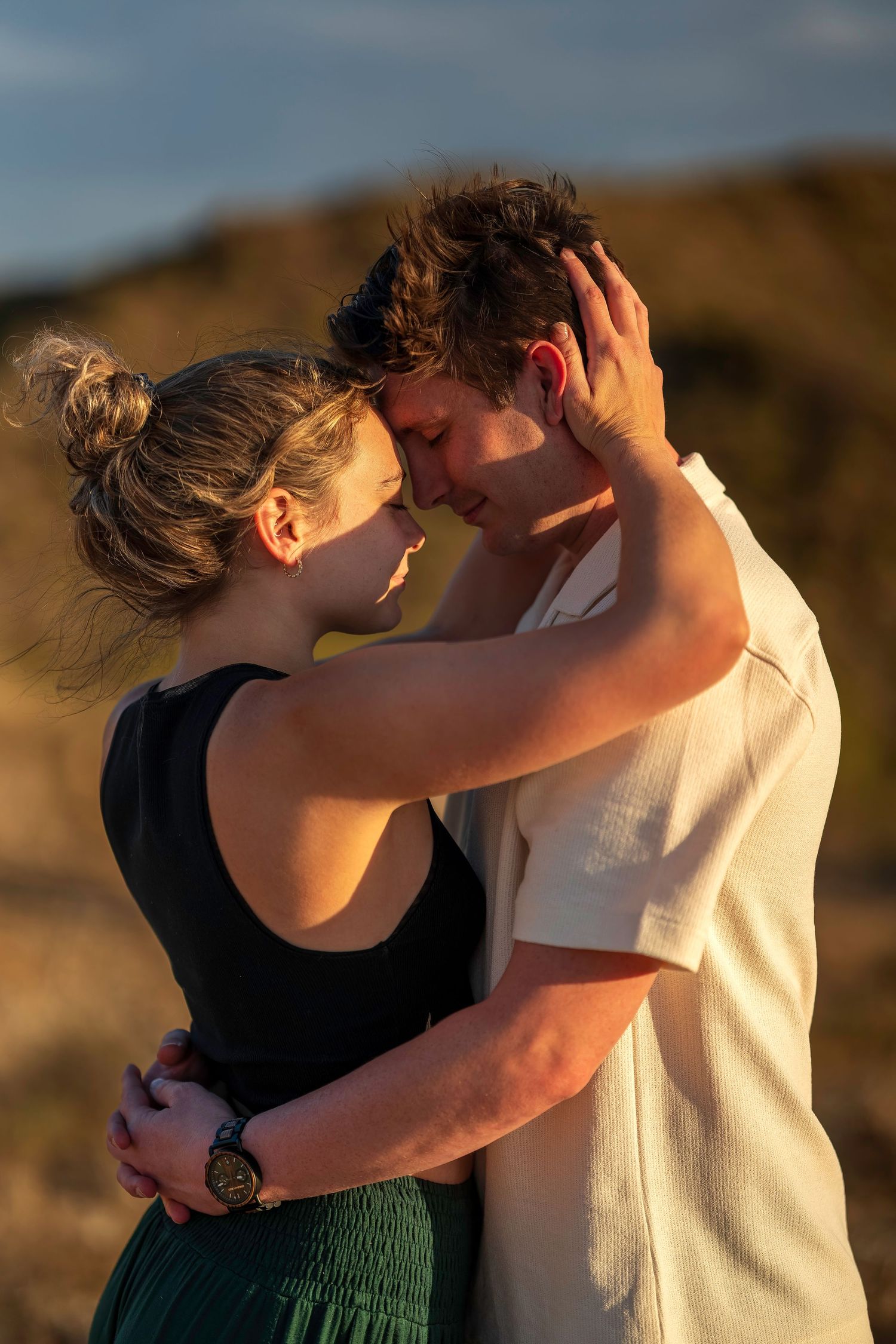 Couple sharing a romantic forehead touch embrace at golden hour outdoors.