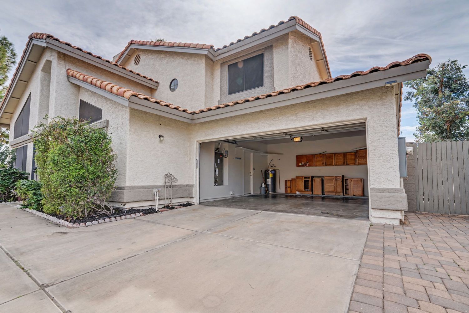 Two-story stucco home with tile roof, open two-car garage, and concrete driveway in a sunny residential neighborhood.