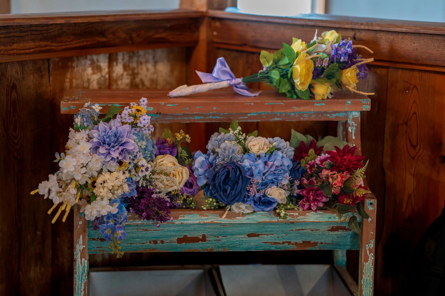 Colorful wedding bouquets with hydrangeas and mixed flowers displayed on a rustic vintage teal wooden bench.