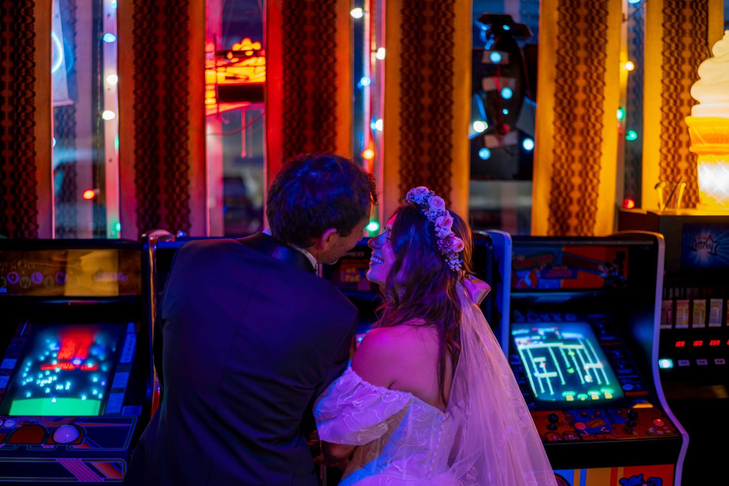 Bride and groom share a romantic moment in front of colorful arcade machines at a unique casino wedding venue.