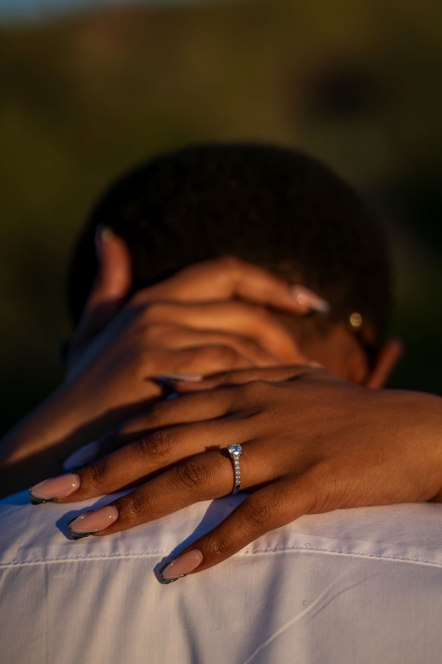 Newly engaged woman showing her diamond ring while embracing her partner at sunset.