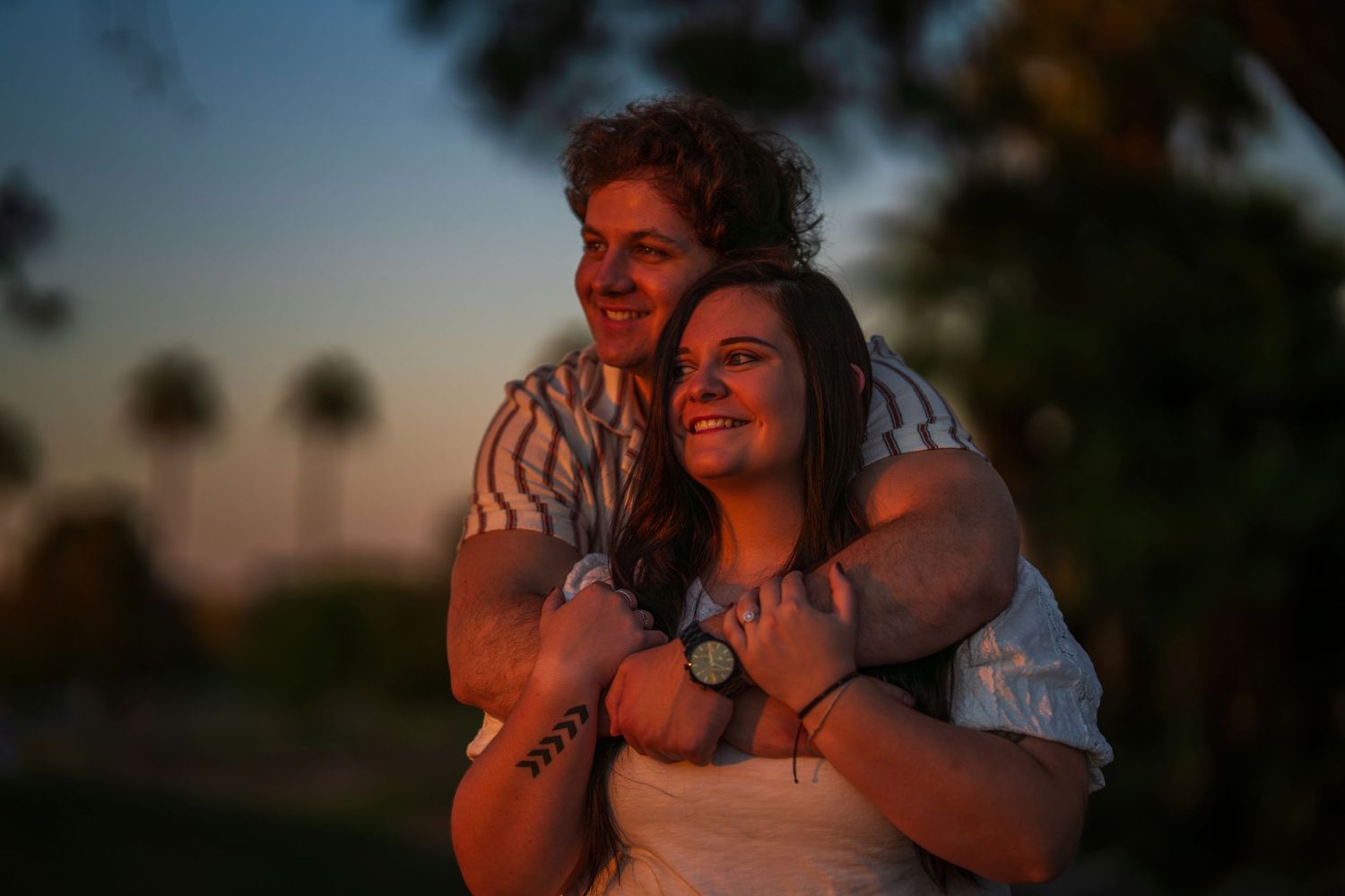 Happy couple embracing at dusk with palm trees silhouetted against colorful twilight sky.