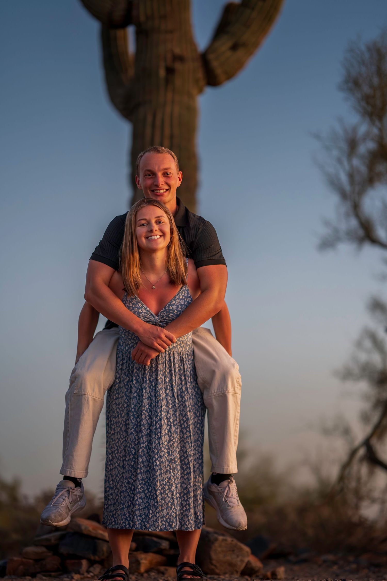 Smiling couple posing together in front of saguaro cactus at golden hour.