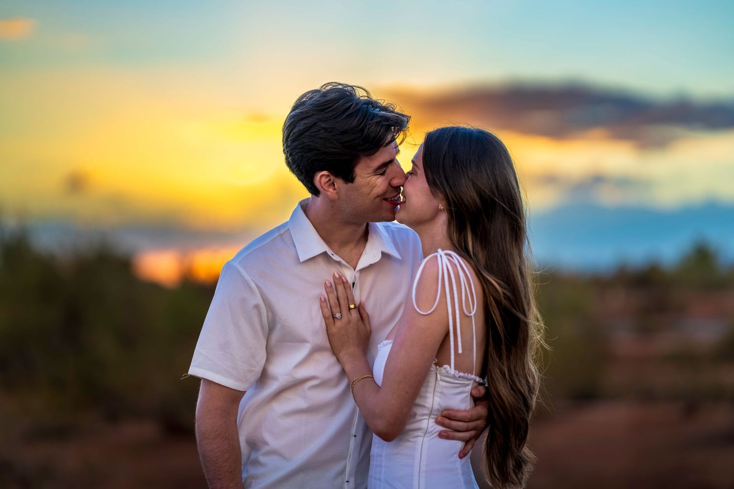 A romantic moment captured between a couple in white outfits during a desert sunset.